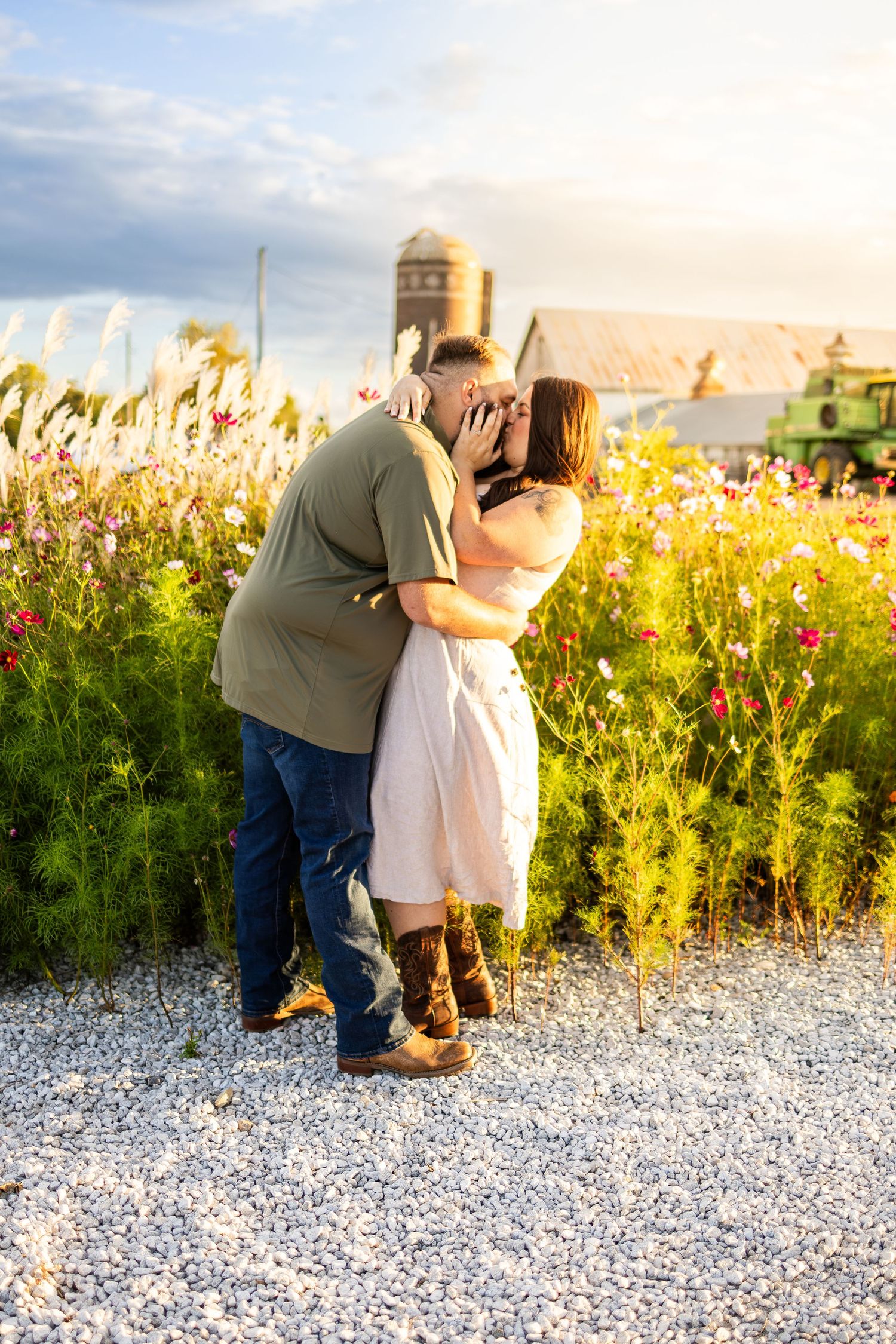 Romantic couple sharing an intimate moment in a wildflower field at sunset near a farm silo.