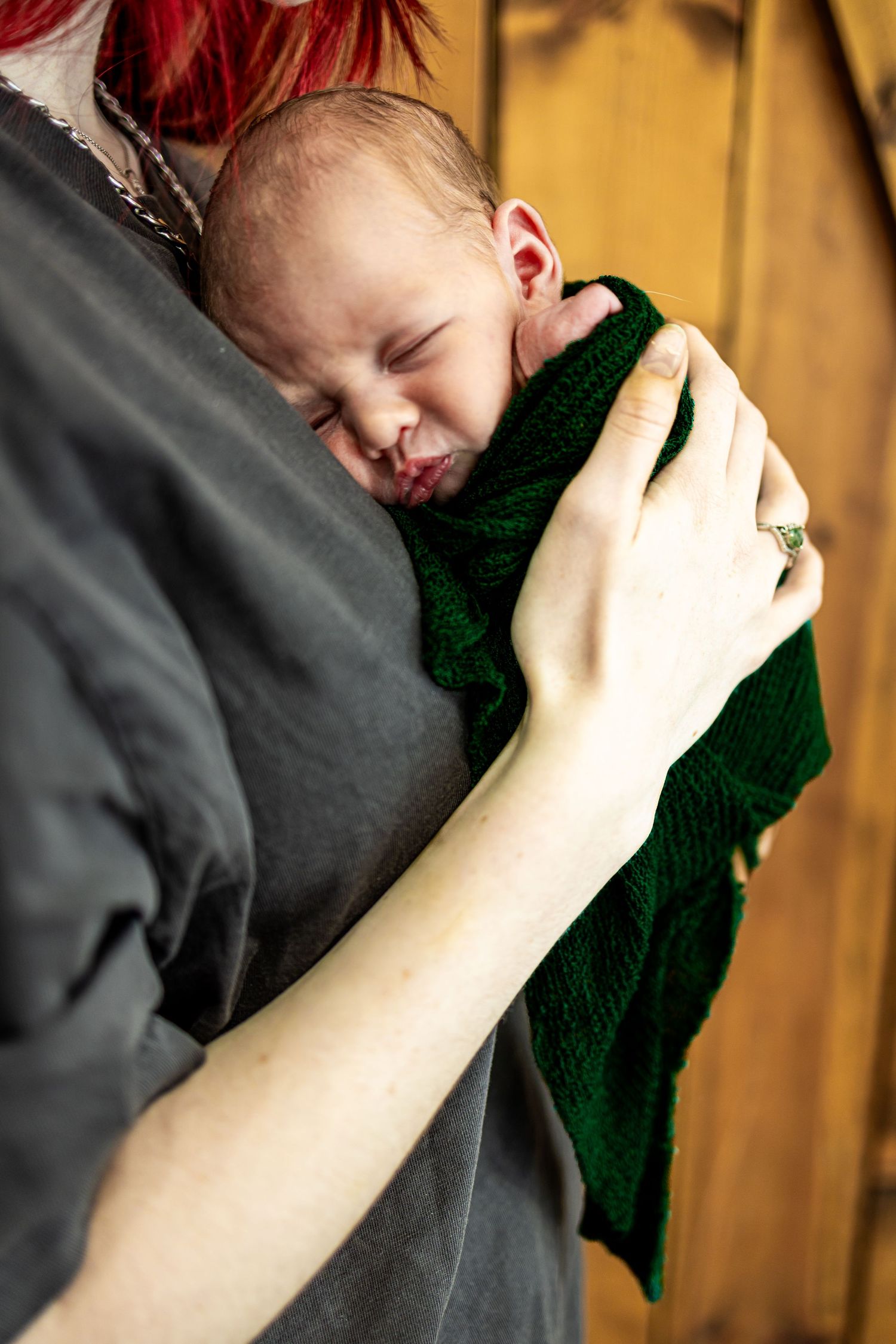 A newborn baby sleeping peacefully in a parent's arms, wrapped in a green knit blanket.