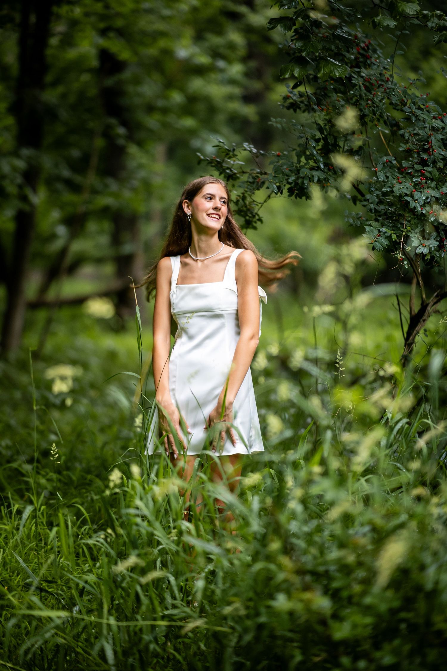 Young woman in white sundress smiling joyfully in a lush garden setting.