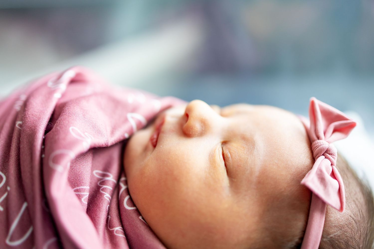 Peaceful sleeping newborn baby wearing pink bow headband in soft focus.