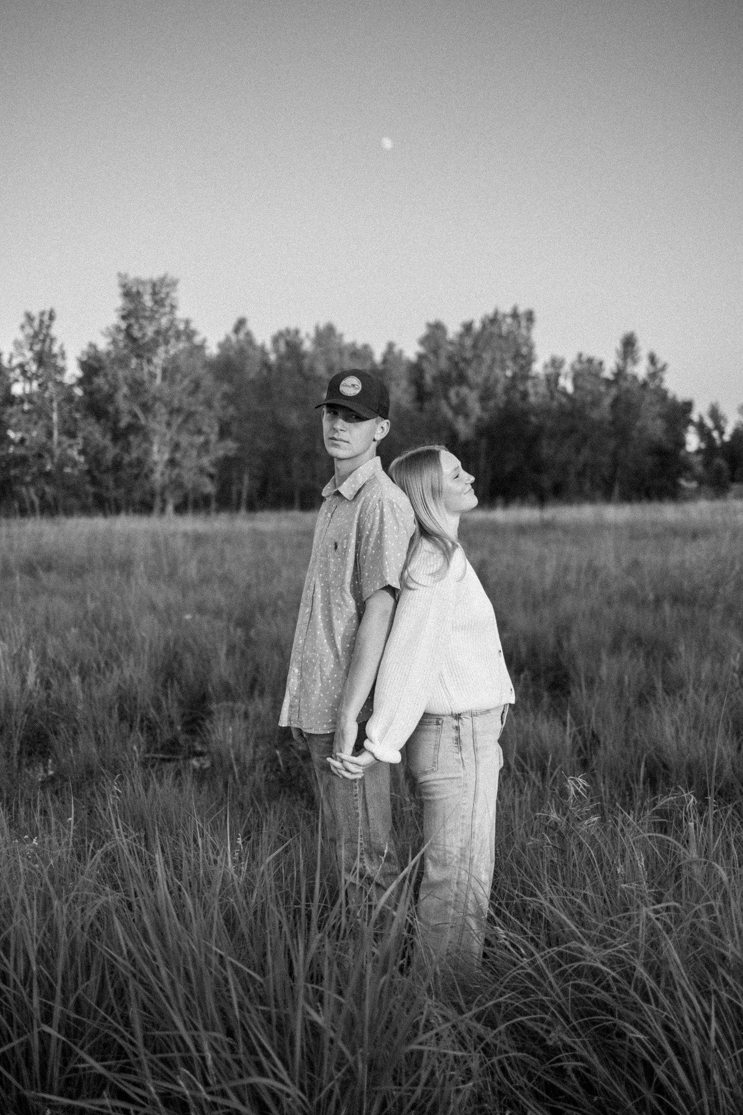 Couple standing together in a tall grass field shown in black and white photography.