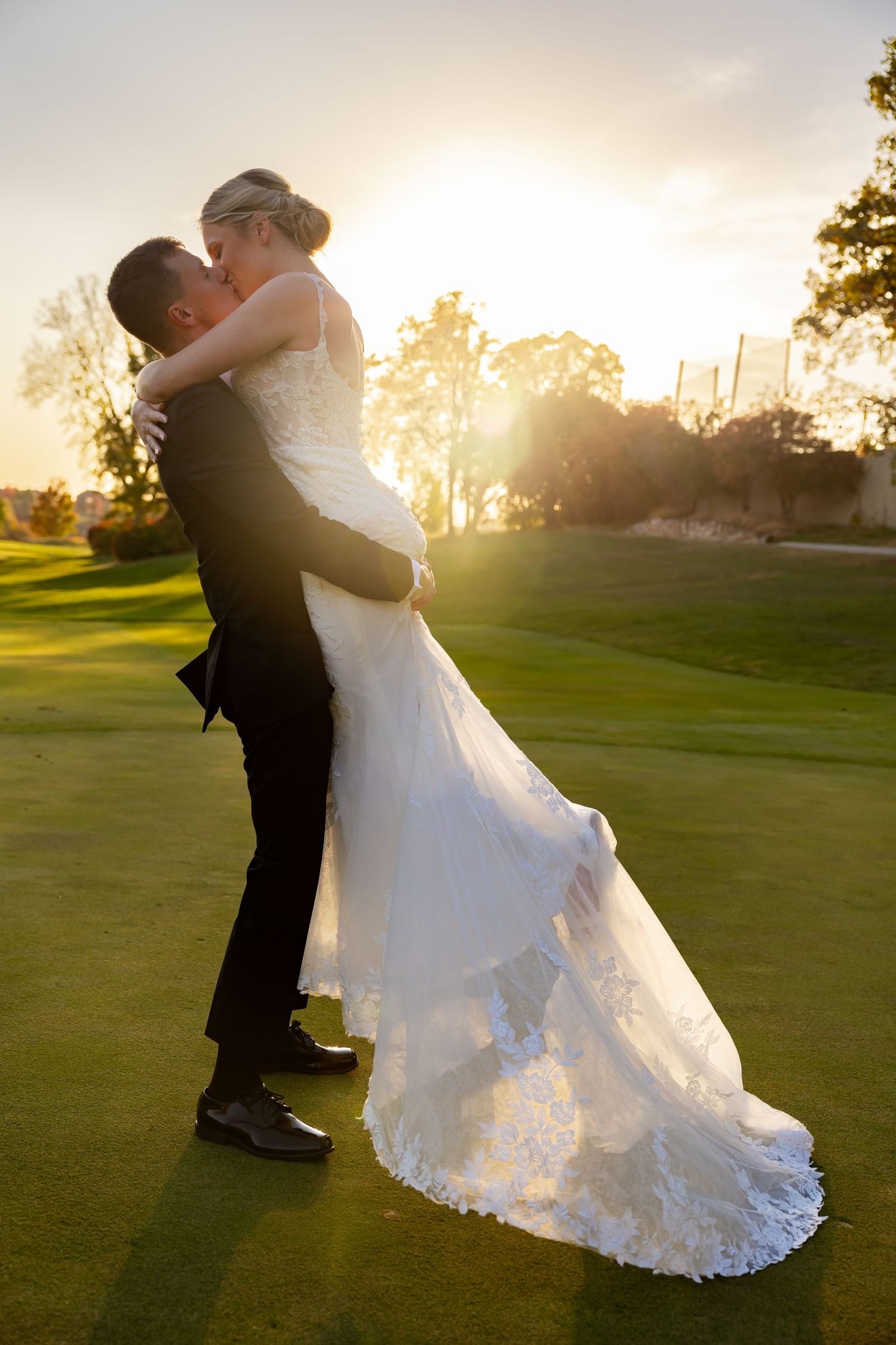 Sunset wedding photo of couple embracing on a golf course with dramatic backlighting.