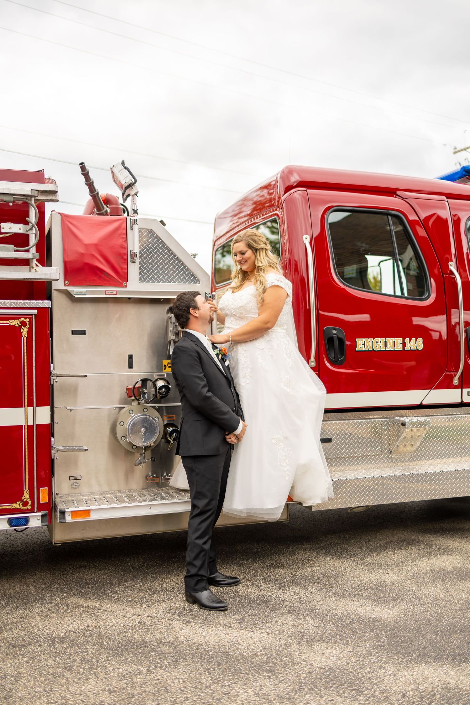 A bride and groom share a romantic moment next to a red fire truck during their wedding photo session.
