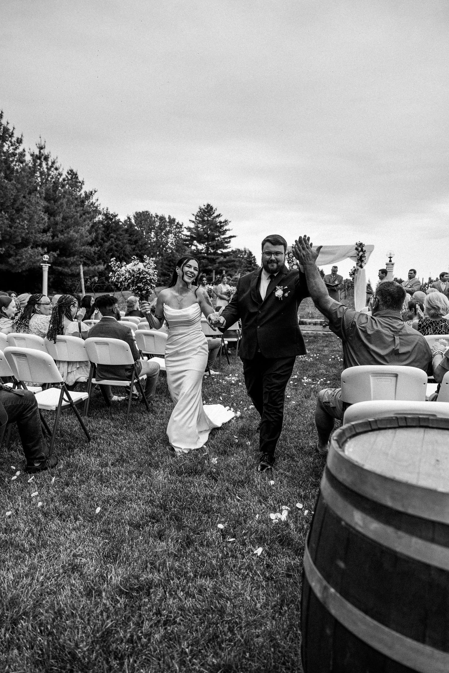 Black and white photo of a joyful bride and groom walking back down the aisle after their outdoor wedding ceremony.