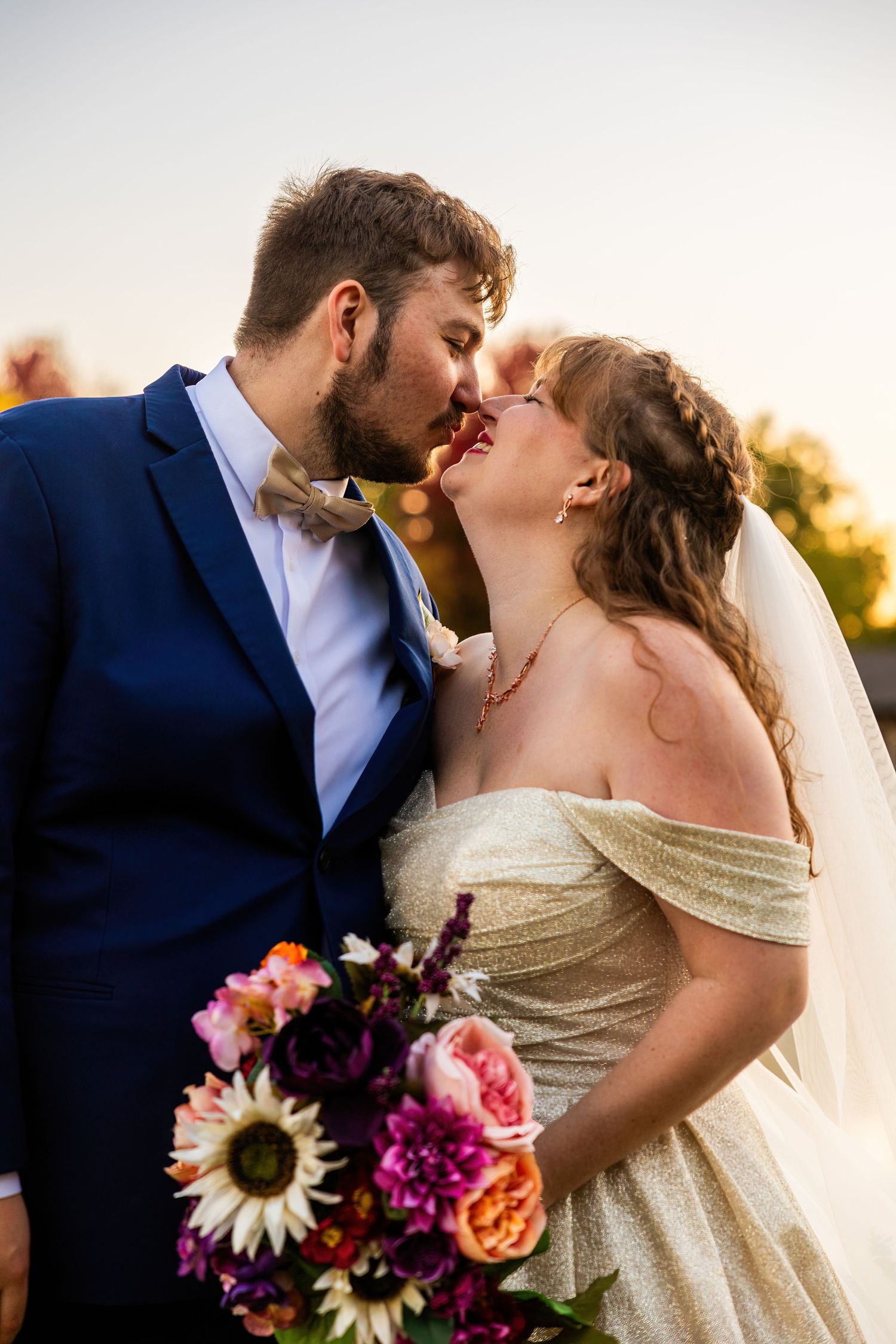 Sunset wedding portrait with vibrant bouquet featuring sunflowers and roses.
