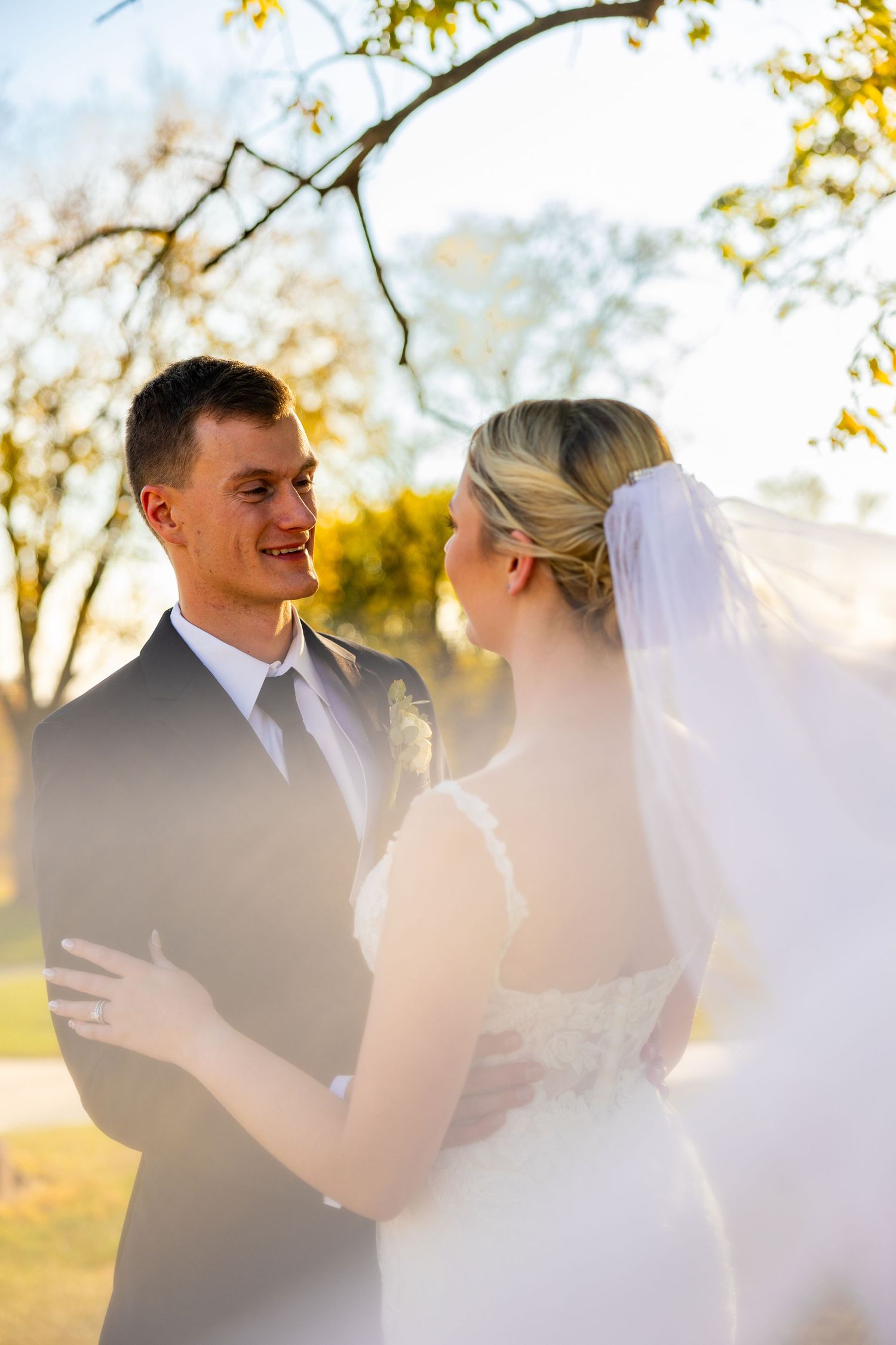 A romantic wedding moment captured in golden sunlight beneath autumn trees.