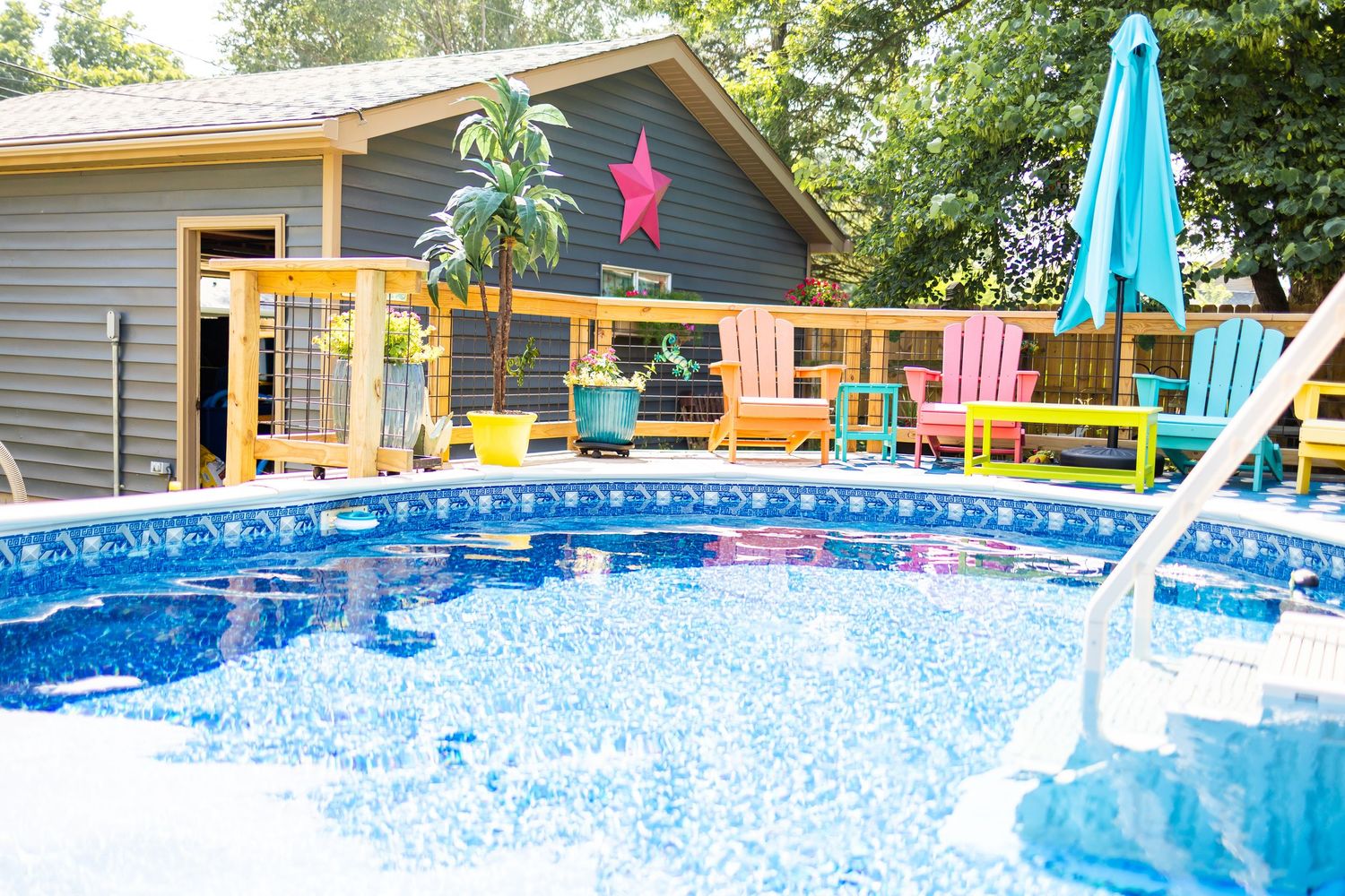 Above ground pool with blue water and colorful pool toys next to a gray house with a wooden deck.