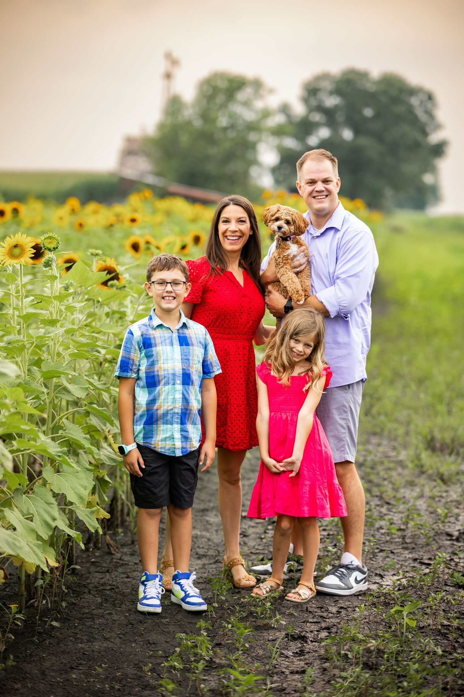 Family portrait with dog among blooming sunflowers in rural setting.