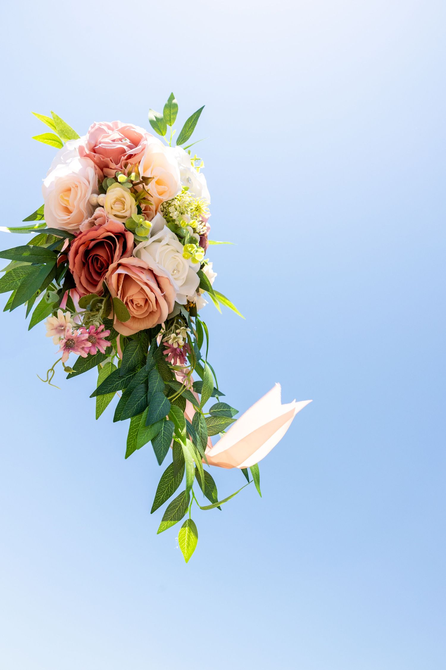 Cascading pink and peach rose bouquet with greenery against blue sky.