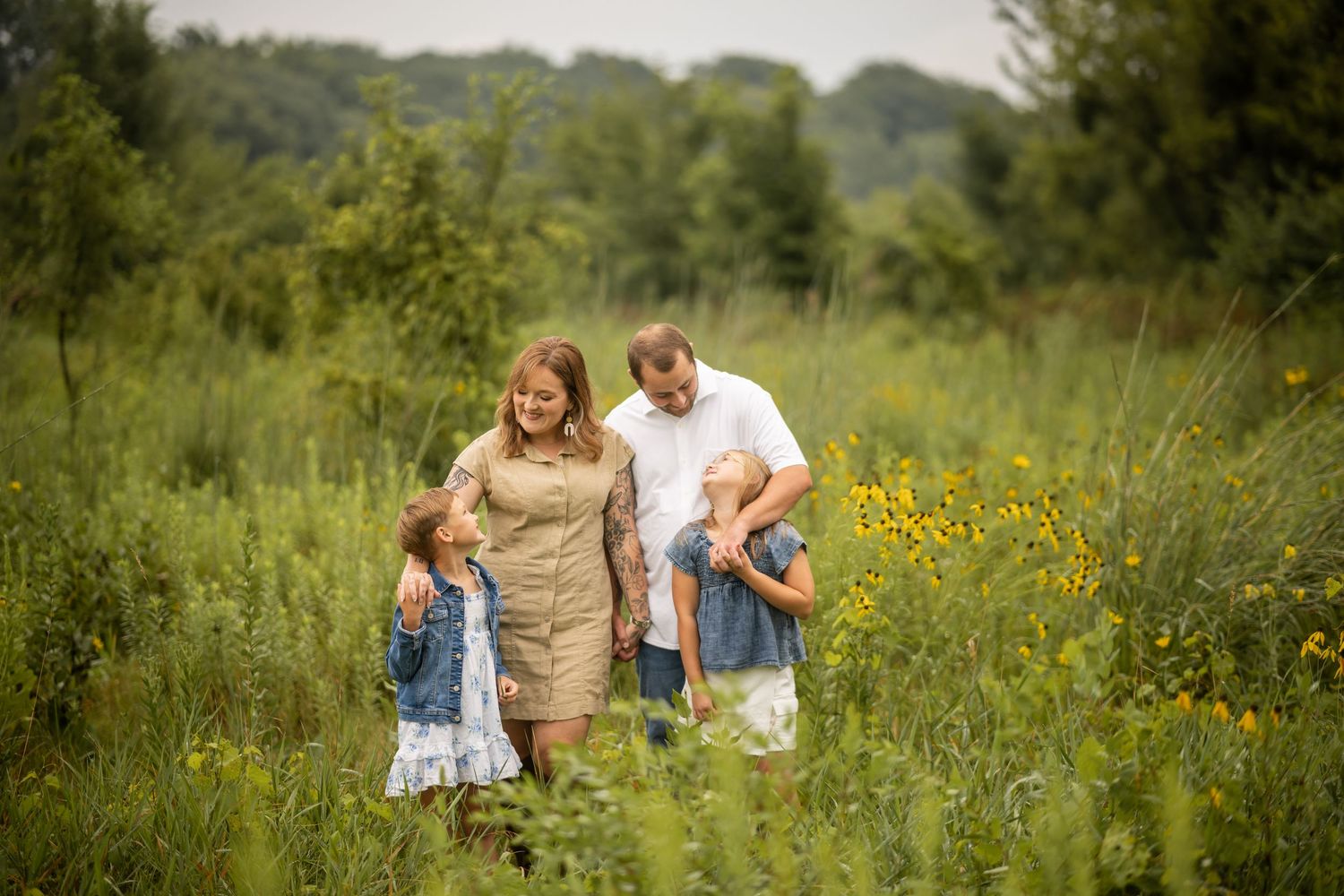 Family of four walking through a lush green meadow with wildflowers on a sunny day.