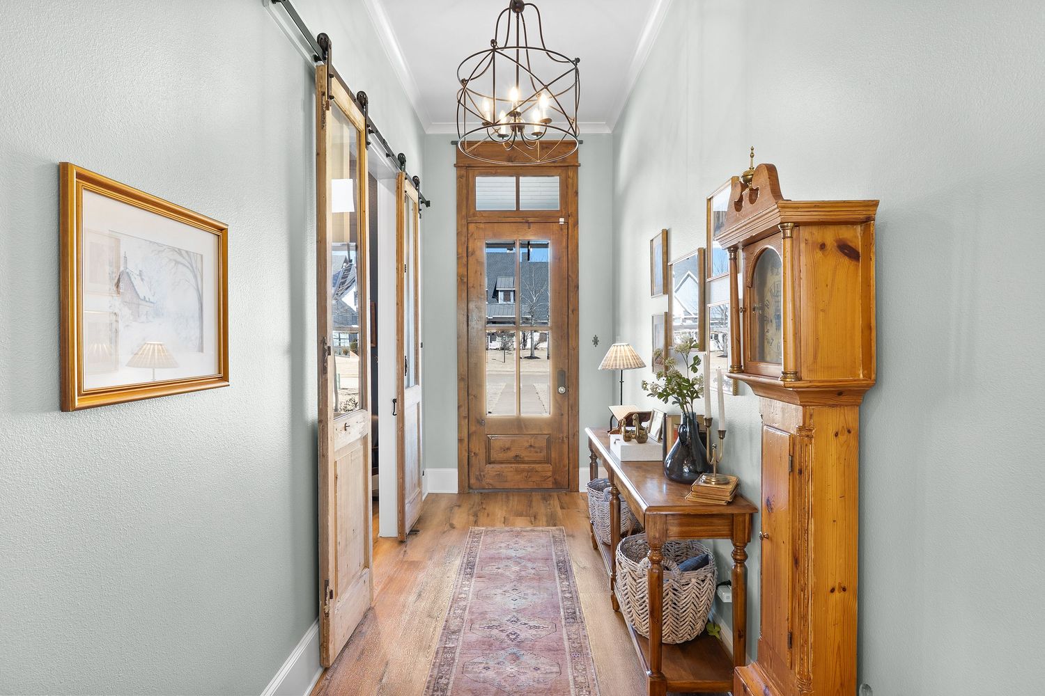 Elegant hallway with barn doors, hardwood floors, Persian rug, pine cabinet, and natural wood front door with transom window.