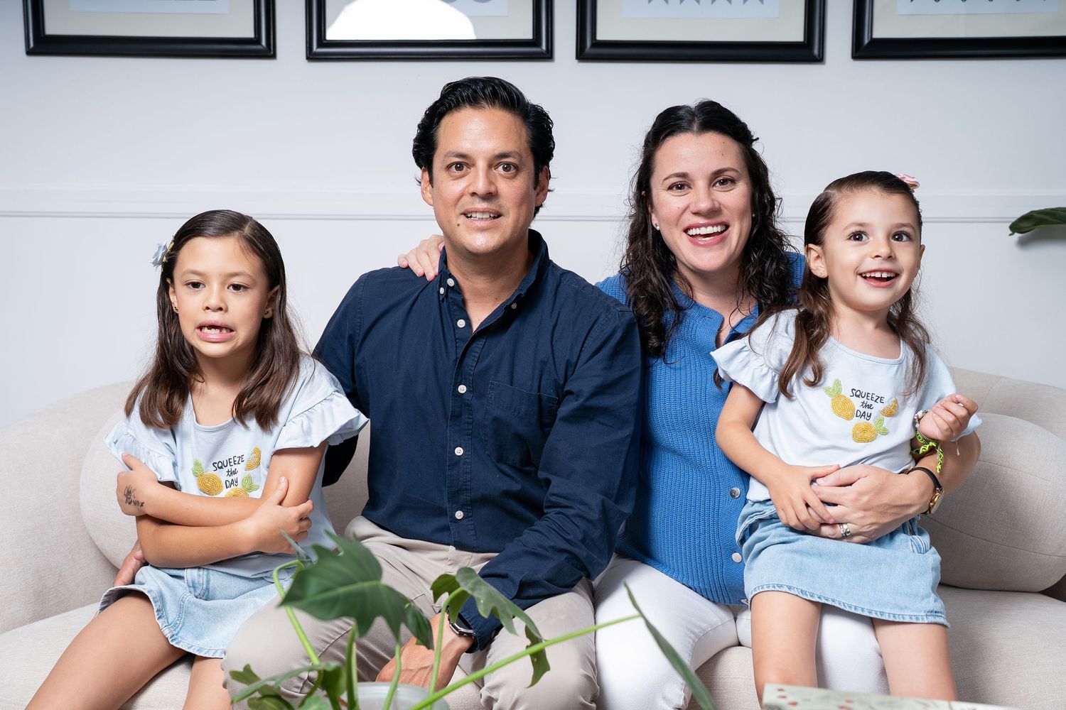 A family poses together on a white couch with decorative frames on the wall.