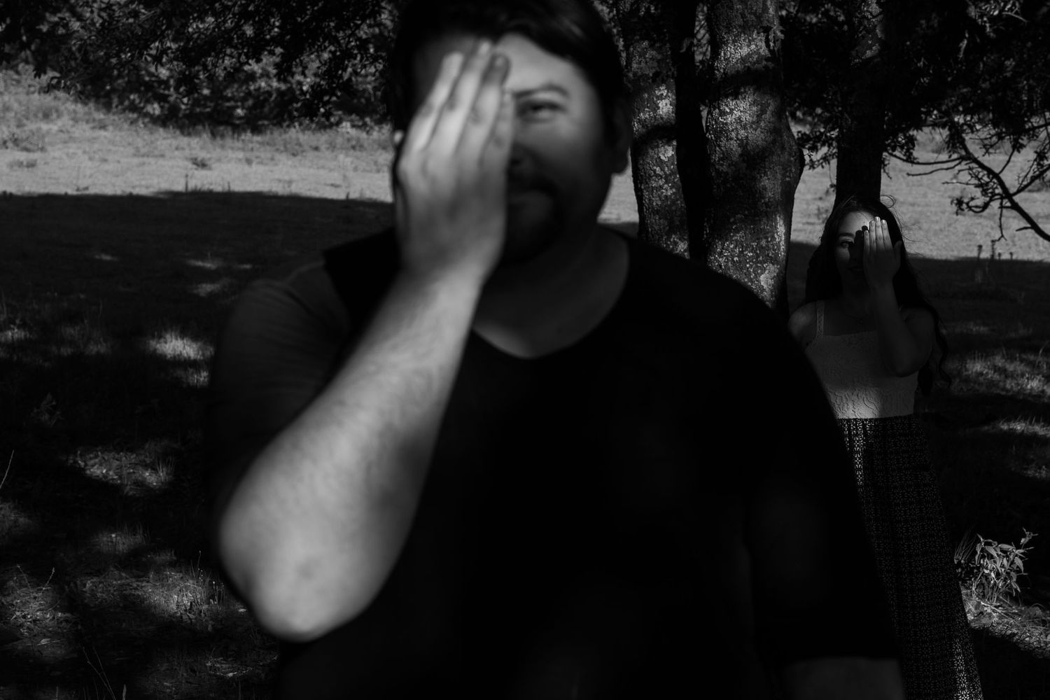 A person in black covering their face with one hand in a moody black and white photo.
