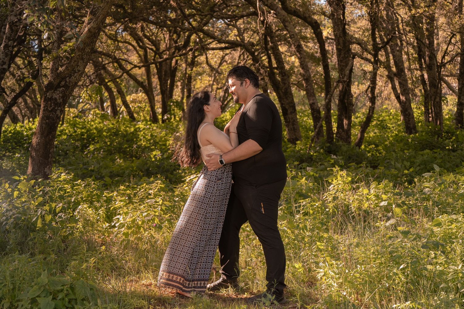 A romantic couple embraces in a sunlit forest with golden wildflowers blooming around them.