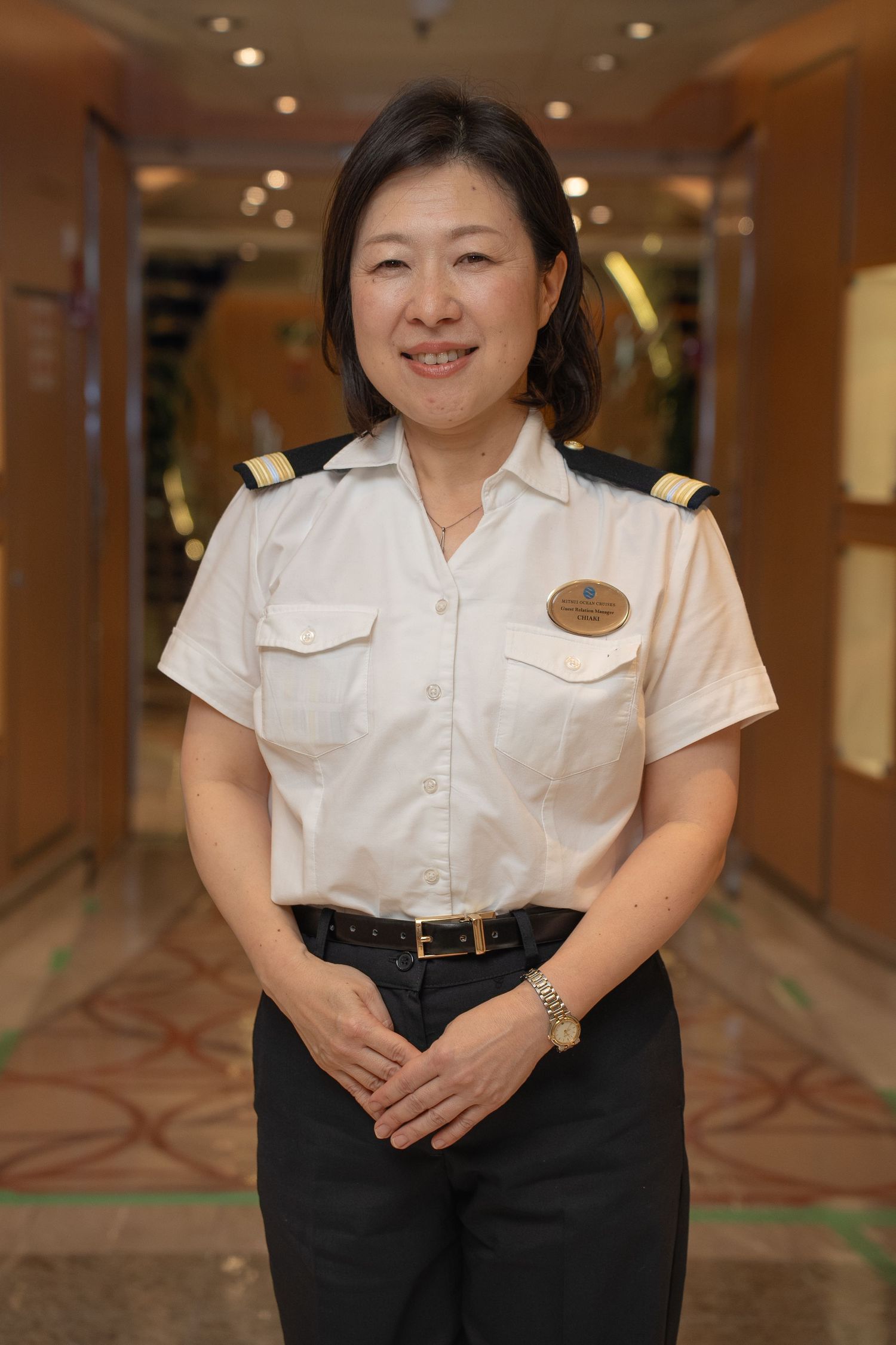 Staff member in white uniform shirt standing in hotel hallway with patterned carpet.