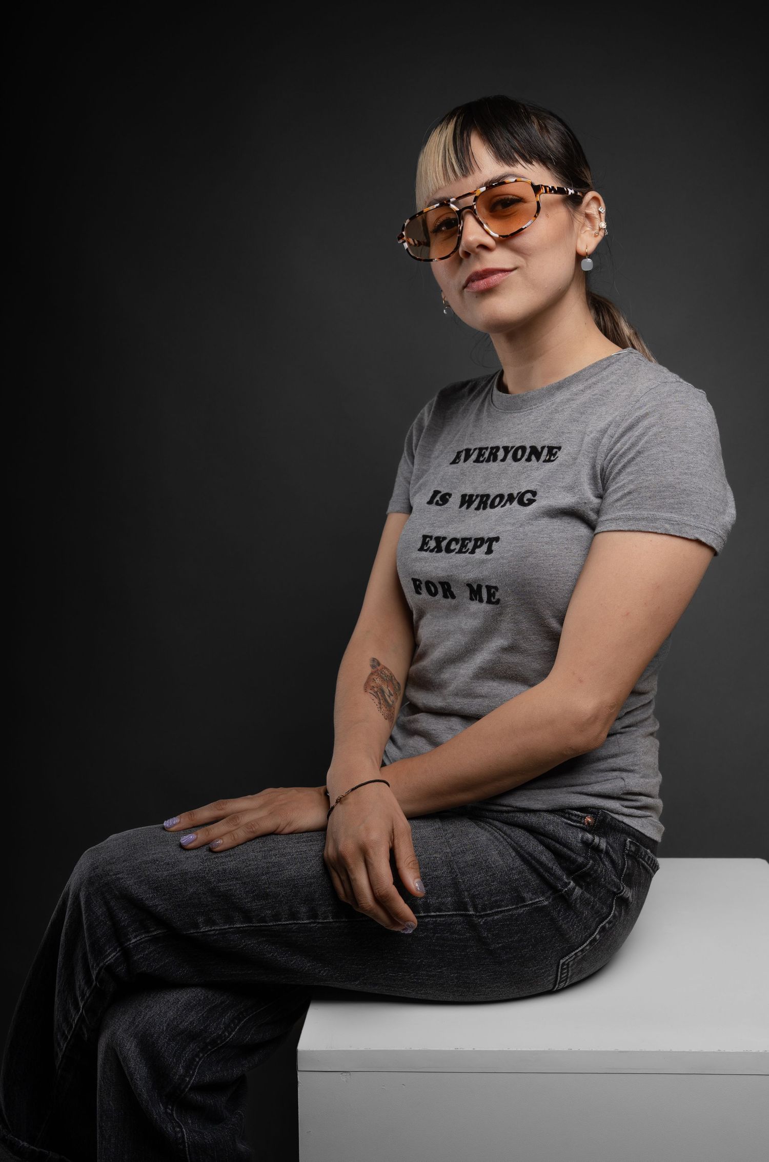 Studio photography series showing person in statement t-shirt sitting on white surface.