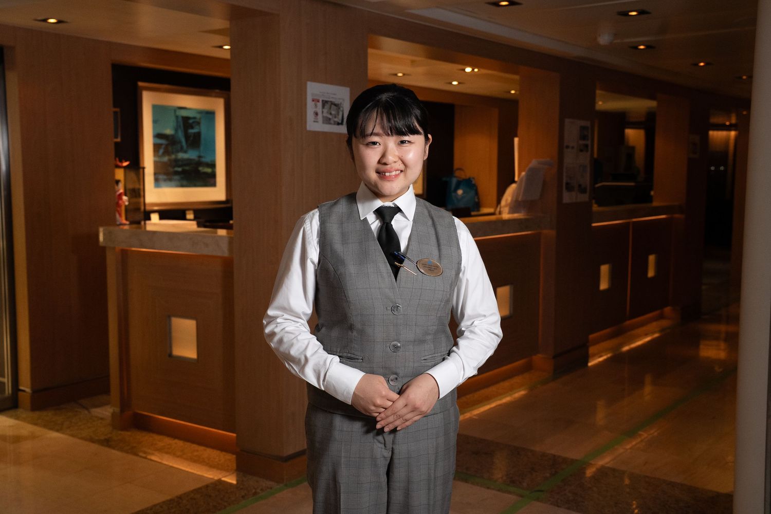 Professional staff member standing in a warmly lit hotel corridor.