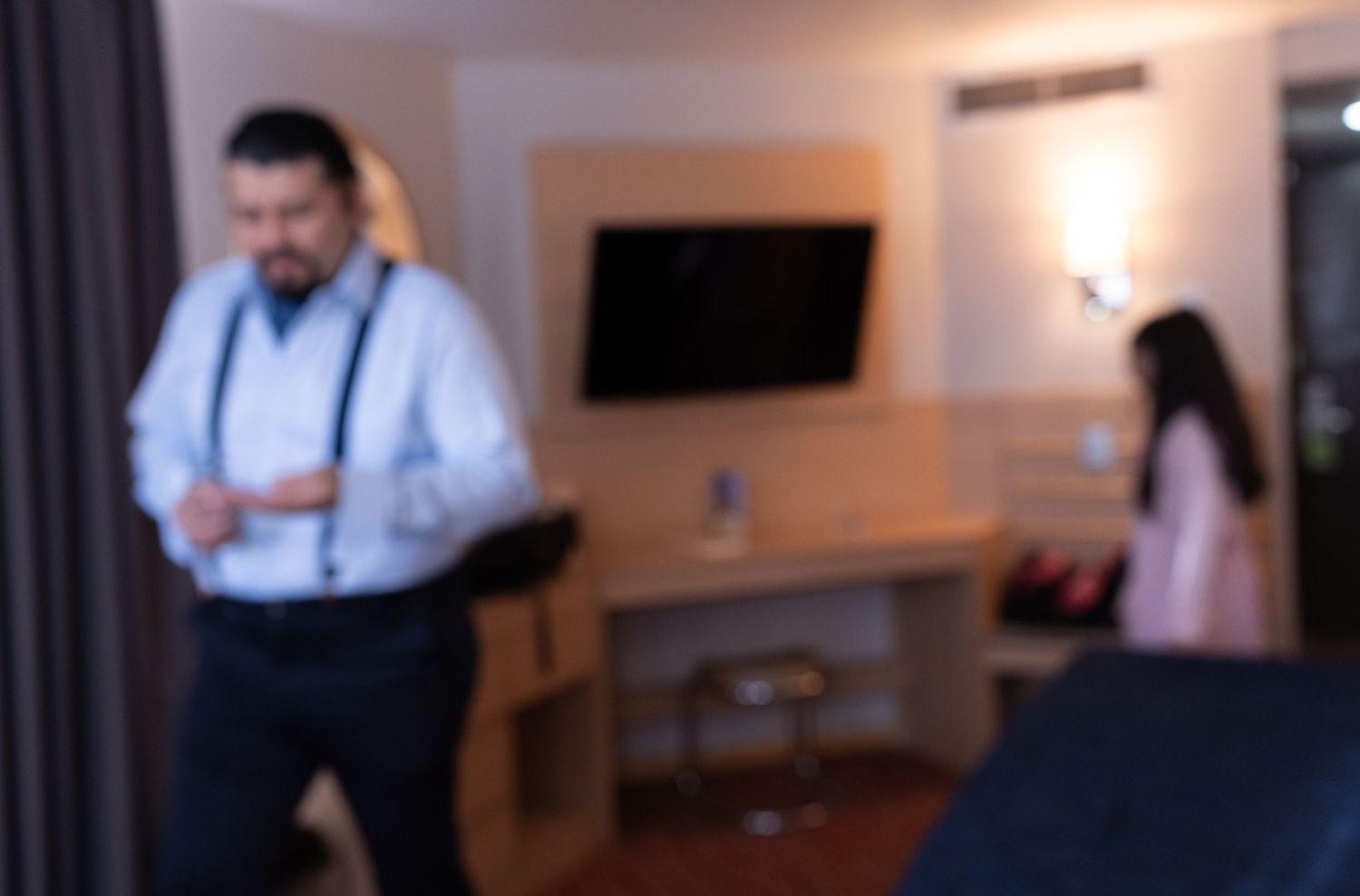 Two people in a hotel room with a mounted TV on the wall and soft lighting creating a casual atmosphere.