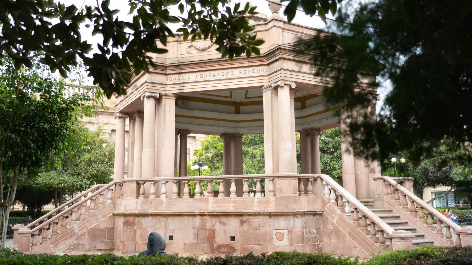 Panoramic view of a historic stone building with ornate columns and grand staircases surrounded by lush trees.