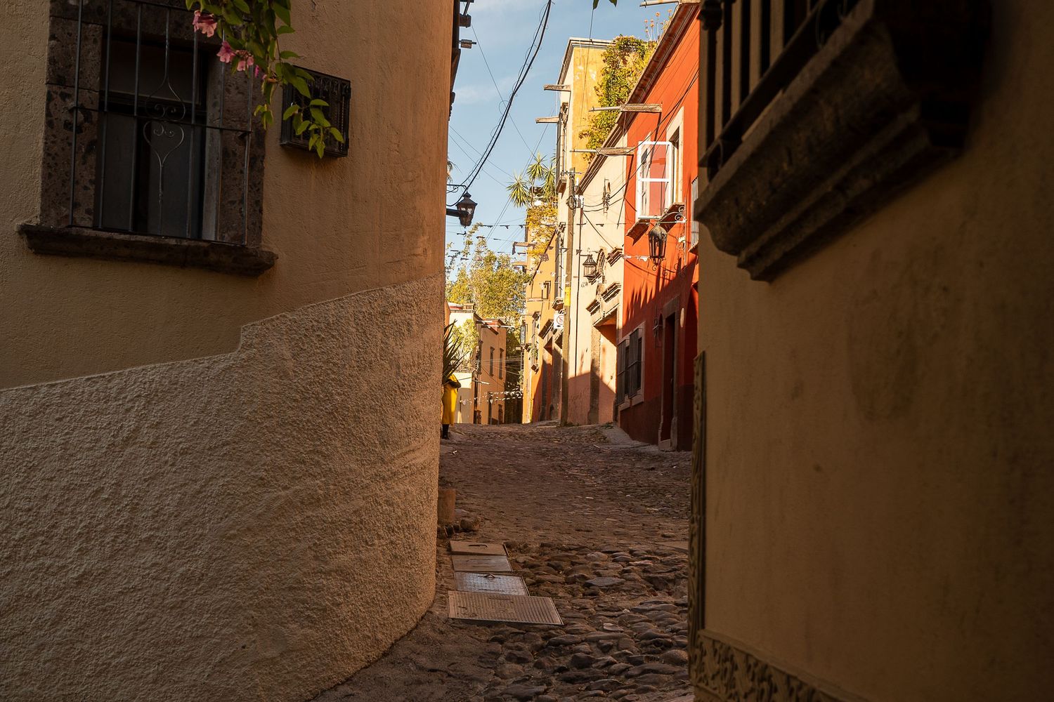 Narrow cobblestone alley between colorful historic buildings bathed in warm golden sunlight in a European old town.
