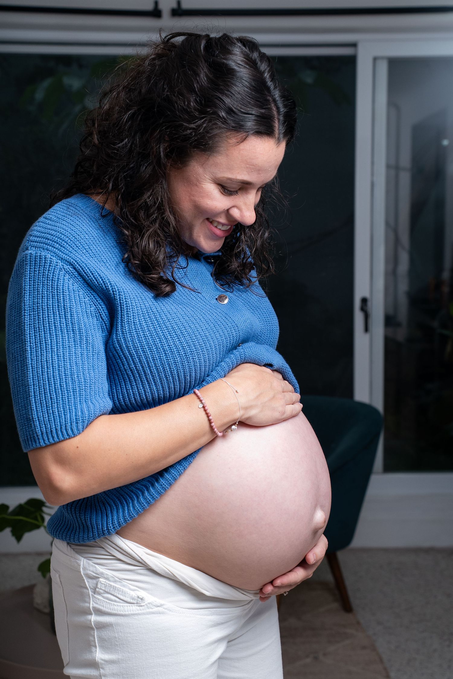 A pregnant woman in a blue sweater cradles her baby bump during a maternity photoshoot.