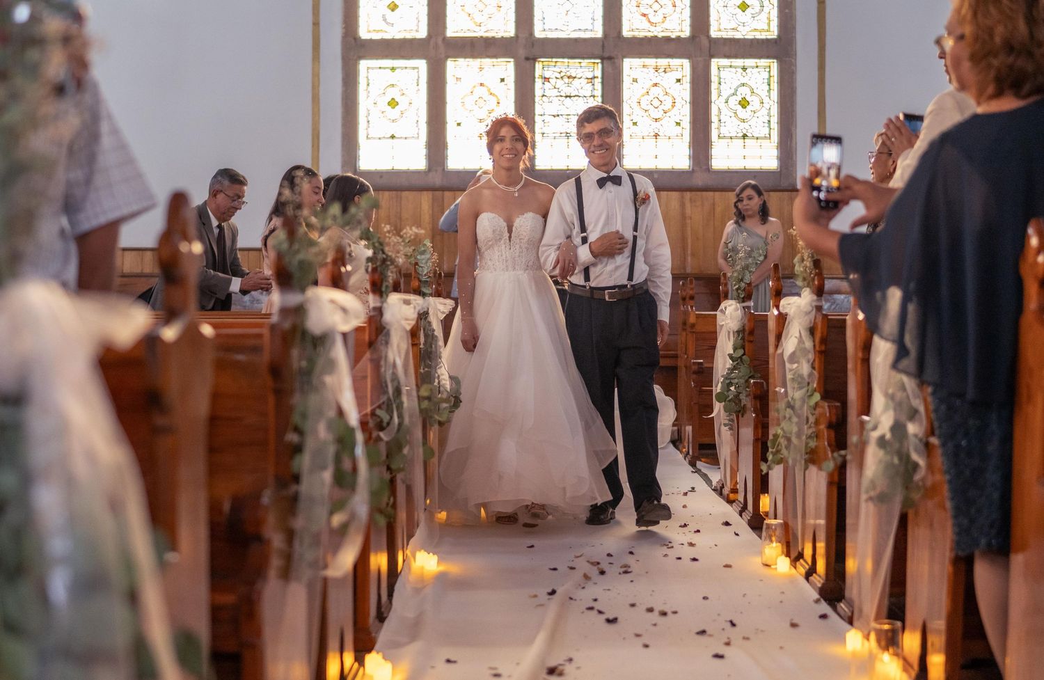 A wedding ceremony in a church with candle-lit aisles and rose petals scattered on the floor.