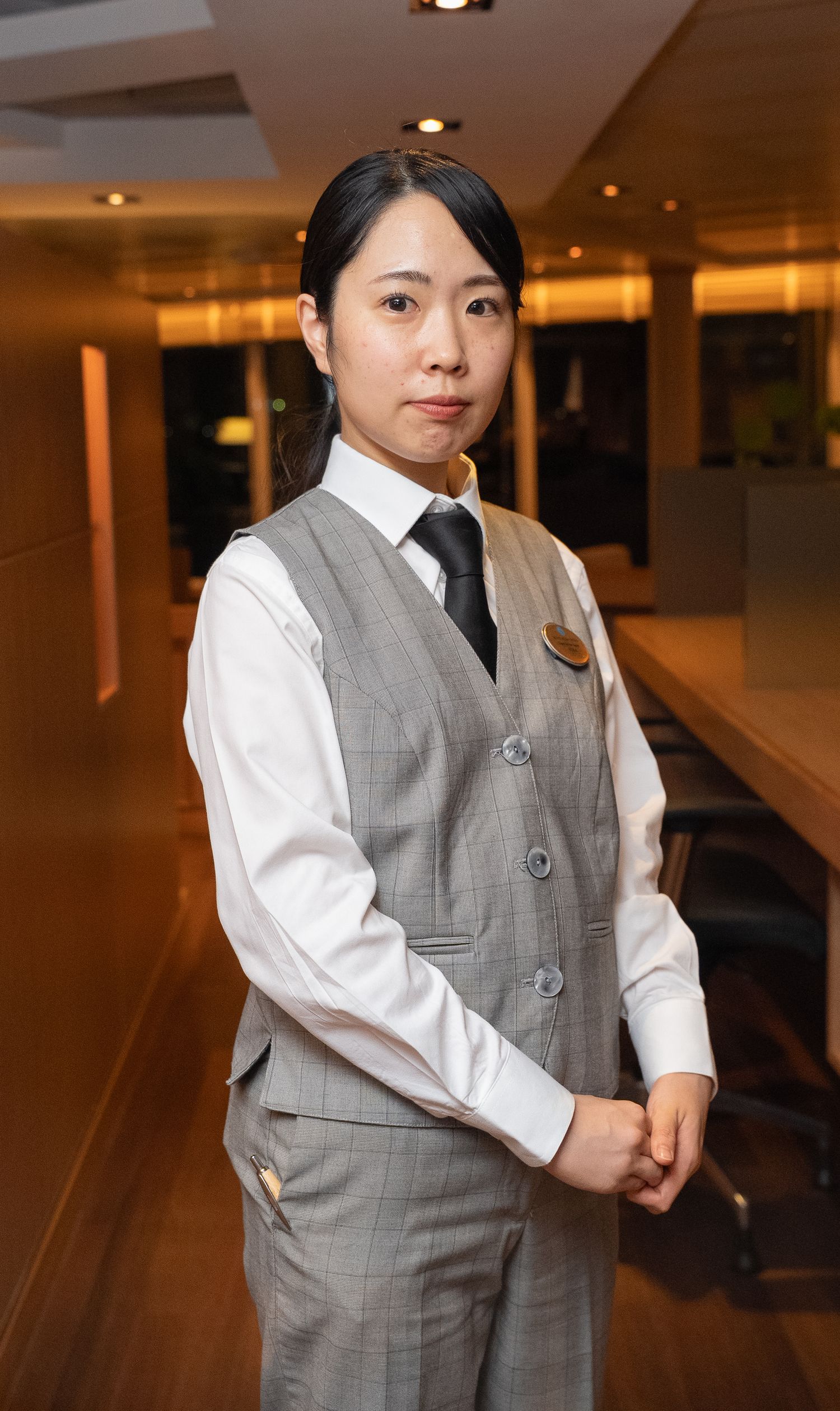 Staff member in professional uniform standing in hotel corridor with warm lighting.