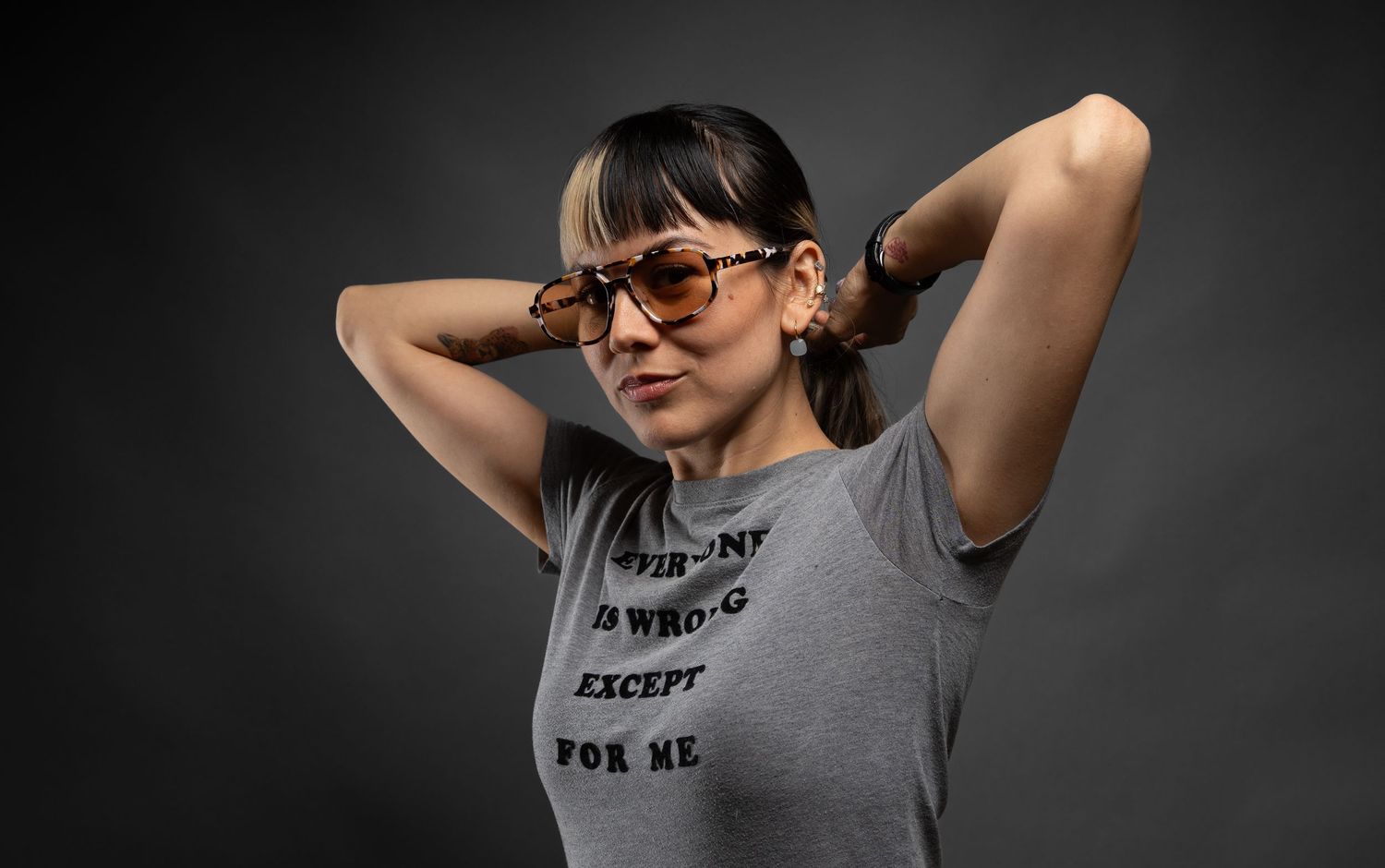Artistic studio shots of person wearing glasses and statement t-shirt in various poses.