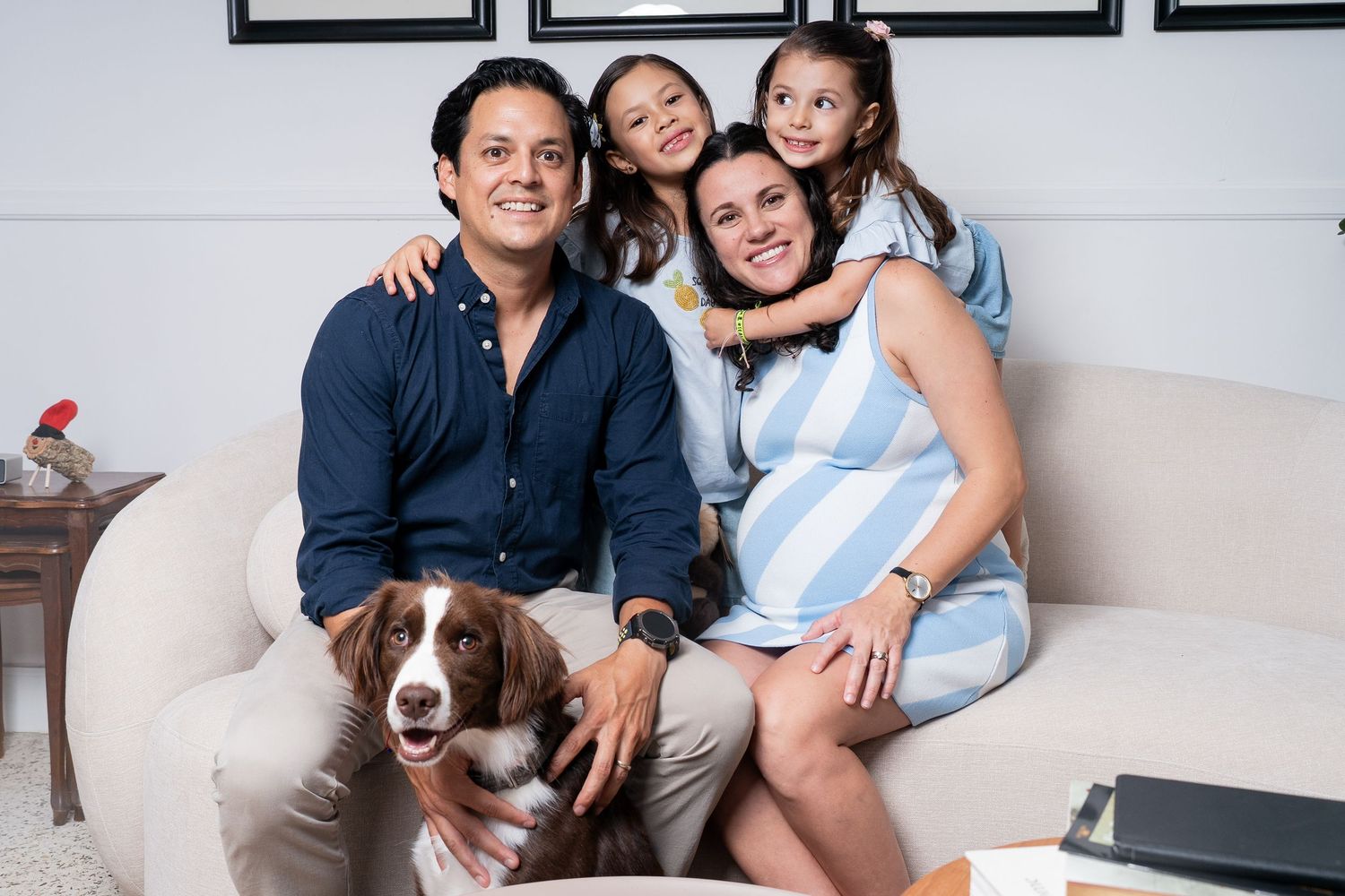 A family poses together on a light colored couch with framed artwork on the wall behind them.