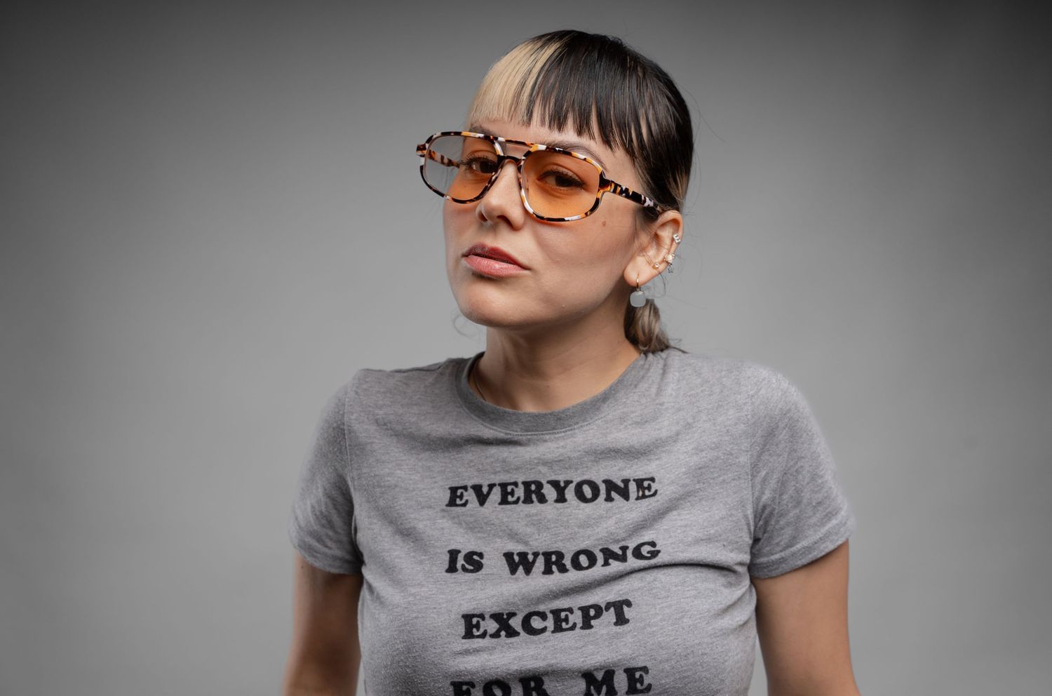 Studio portrait showing person in gray t-shirt with text 'Everyone is wrong except for me' against dark background.