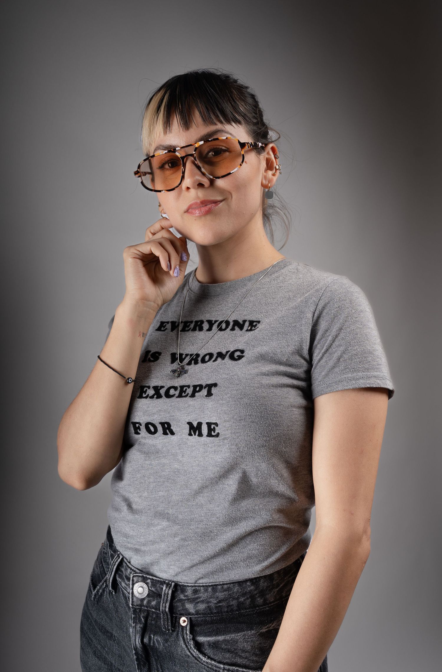 Person in gray t-shirt and jeans striking confident poses against dark studio background.