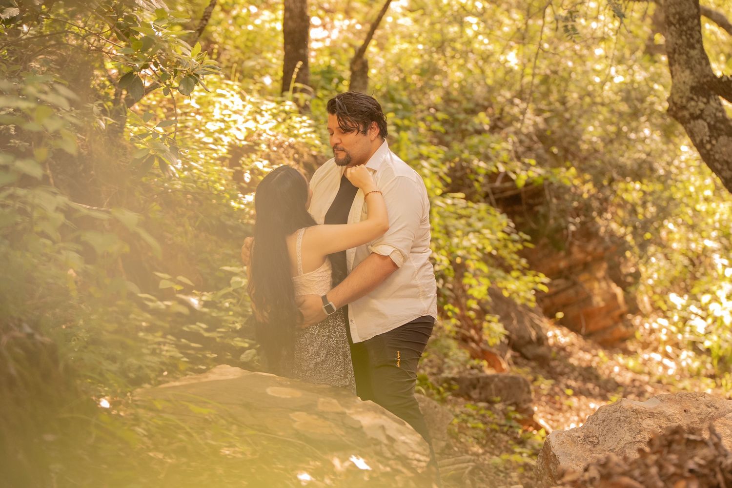 Two people share an intimate dance moment surrounded by trees at sunset.