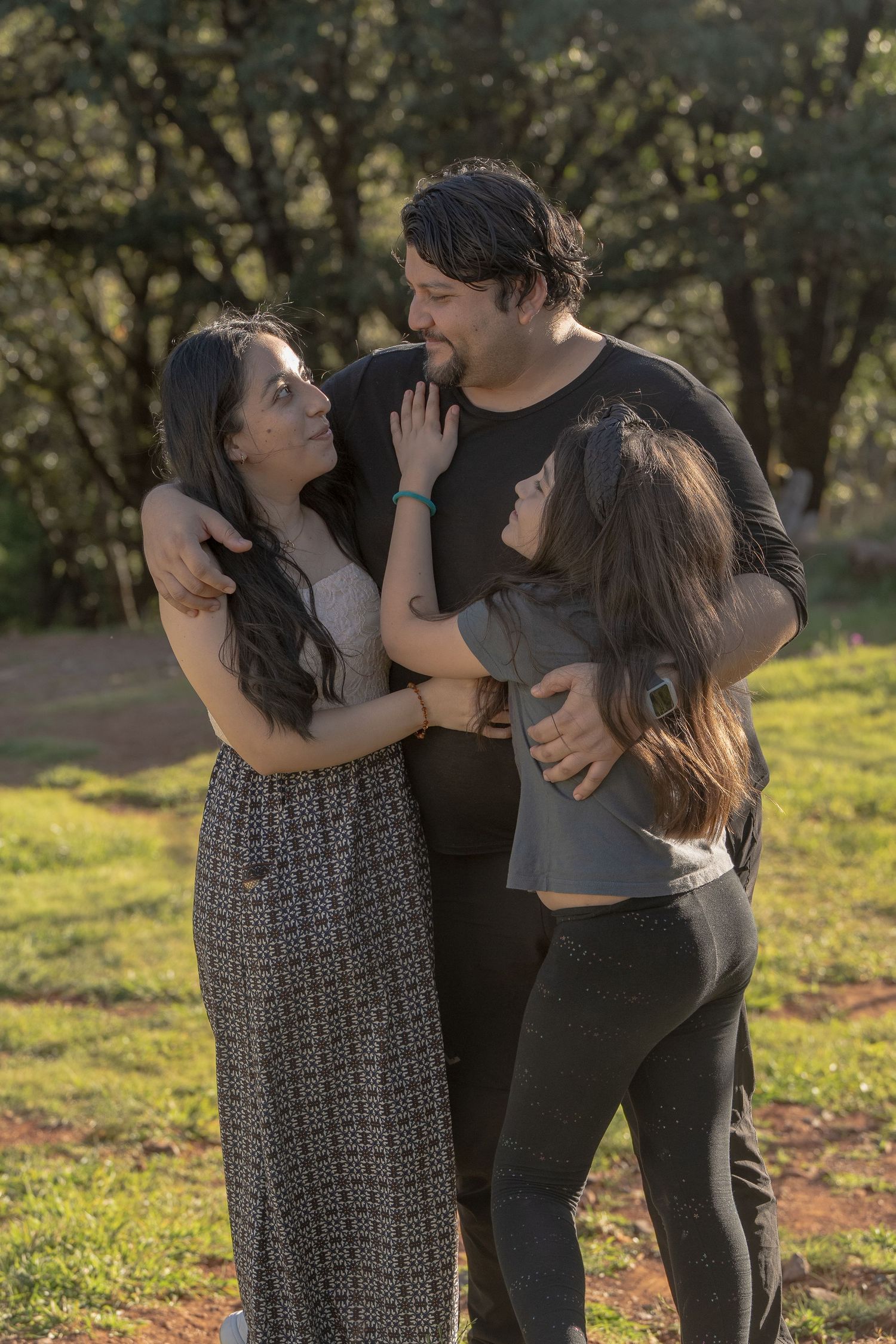 Three people share an intimate moment together outdoors in warm evening light.