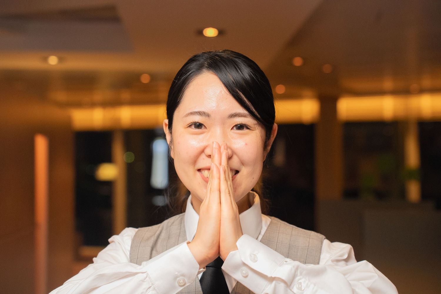 Hospitality worker in uniform poses in hotel hallway with recessed lighting.