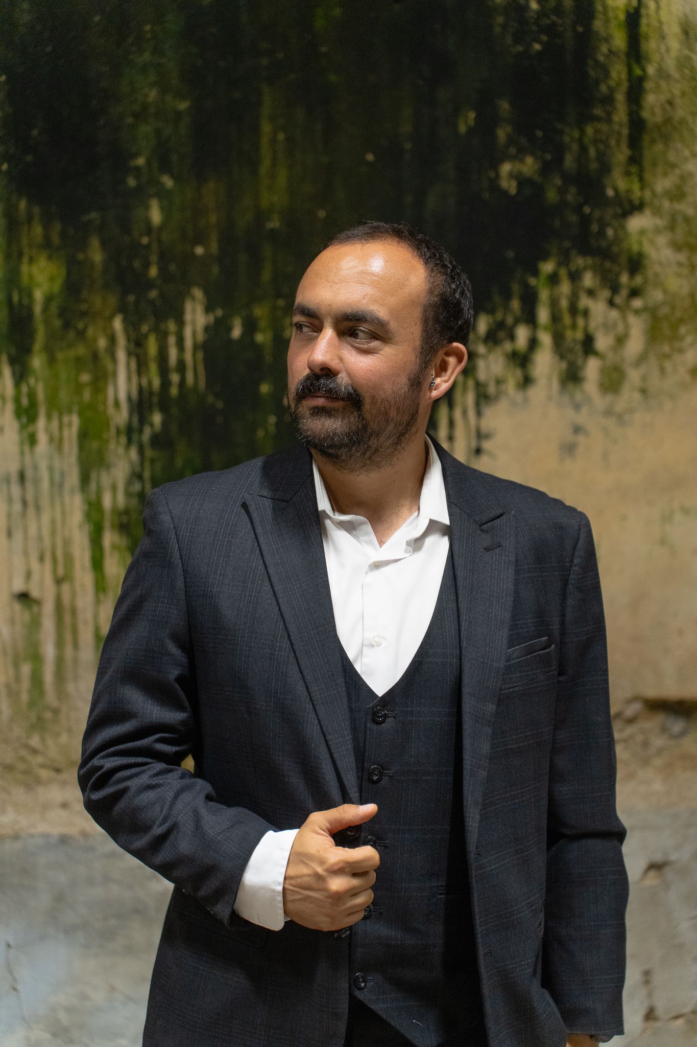 A man in a dark business suit and white shirt stands against a textured wall in a series of poses.
