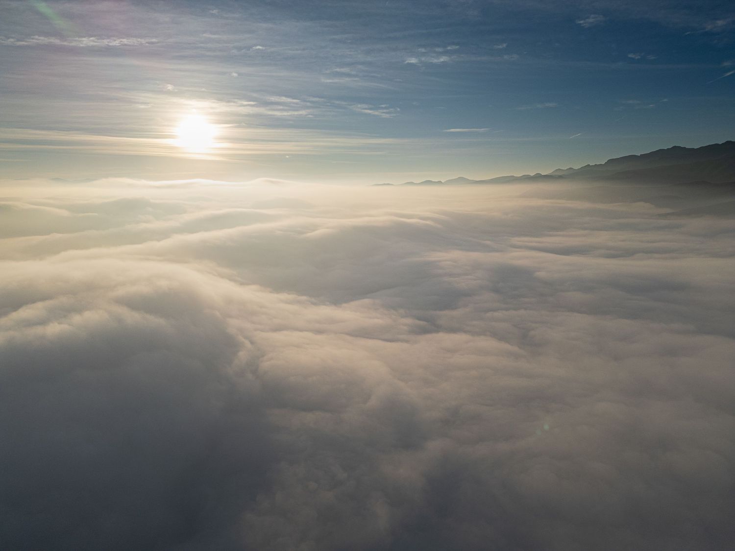 Aerial view of misty clouds during sunset with sunlight streaming through layers of white cloudscape.