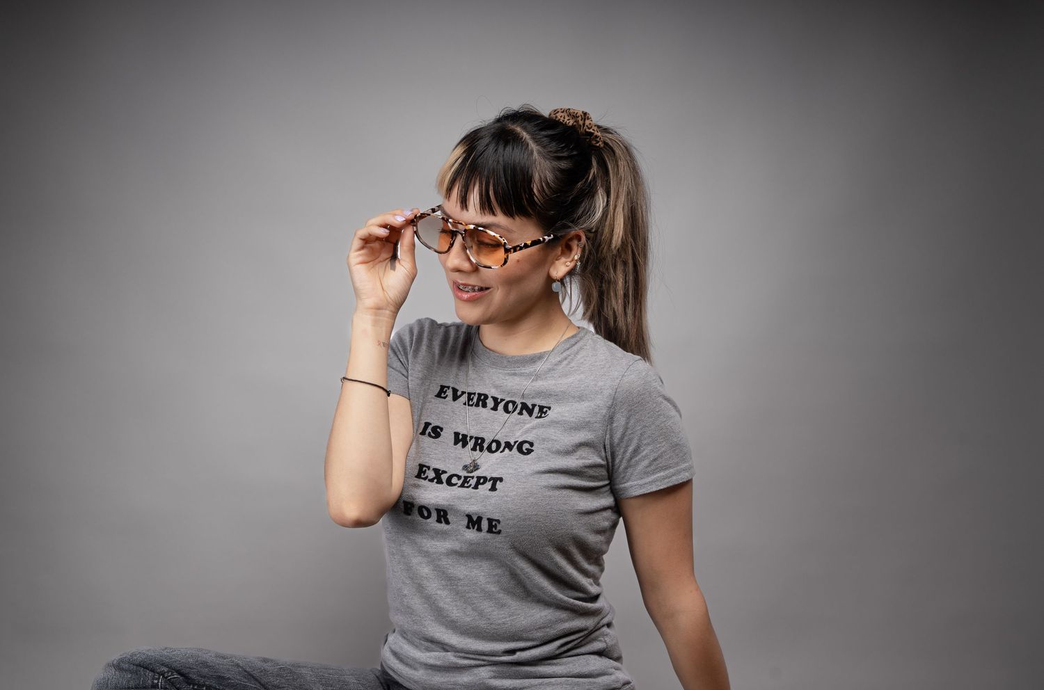 A person wearing glasses and a gray t-shirt poses playfully against a dark backdrop.