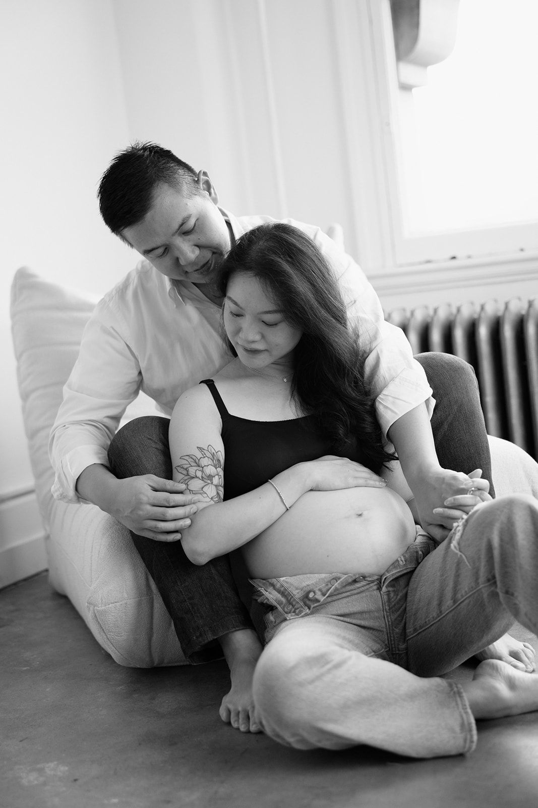 Intimate black and white maternity photo of expectant couple sitting on floor.