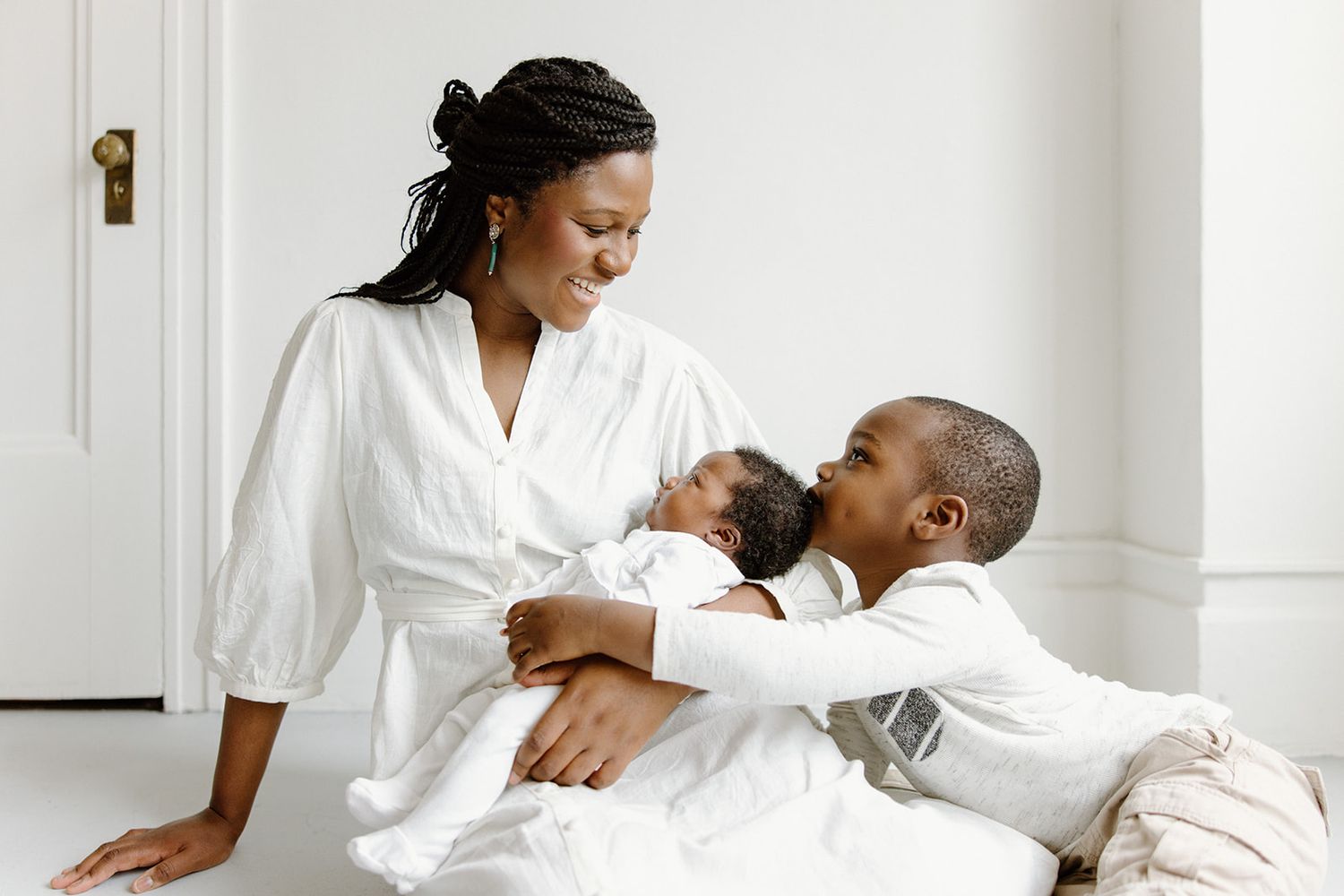 People wearing white outfits sit and laugh together on a bed in a bright, airy room.