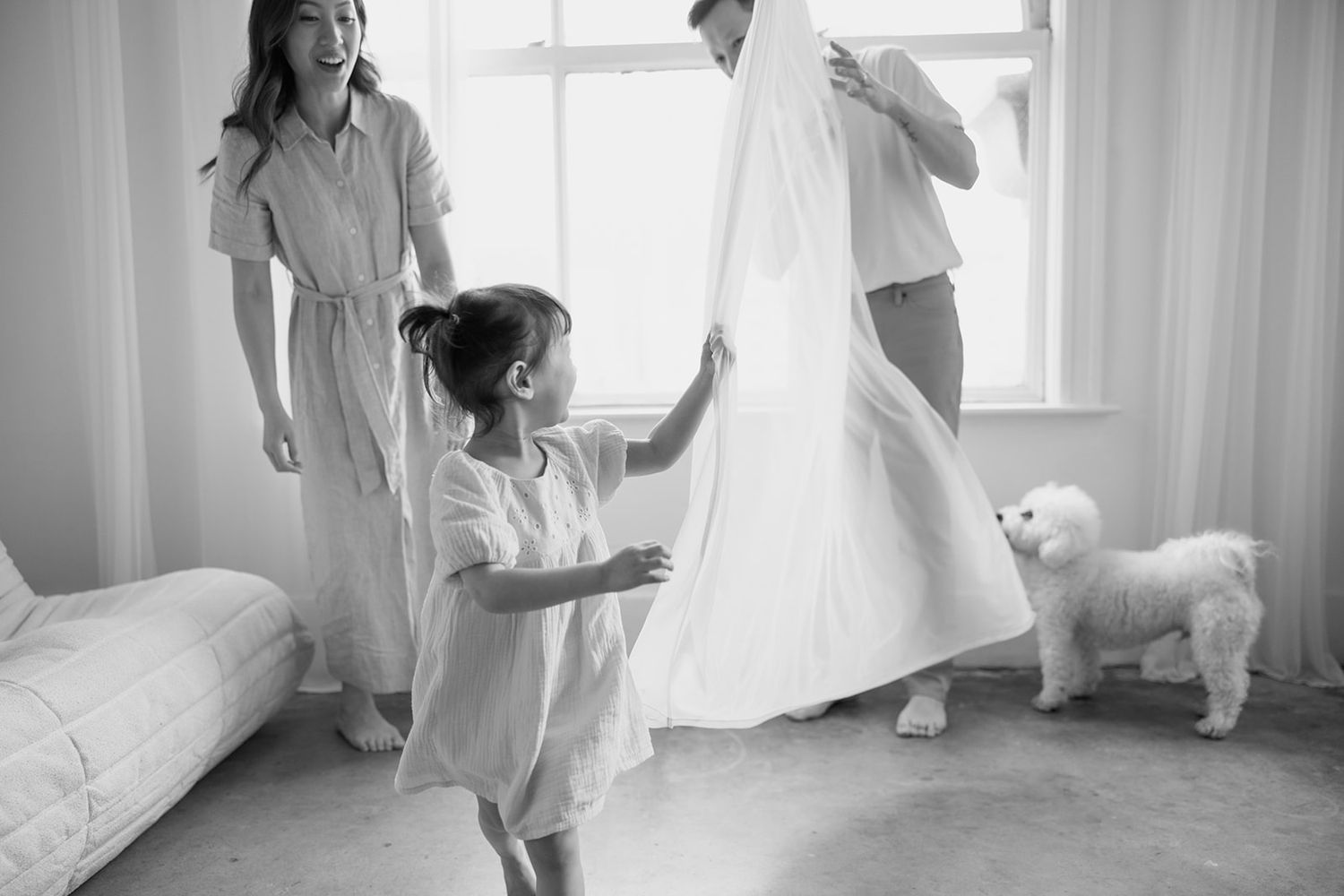 Two people wearing all white clothing dance gracefully in a light-filled room as fabric flows around them.