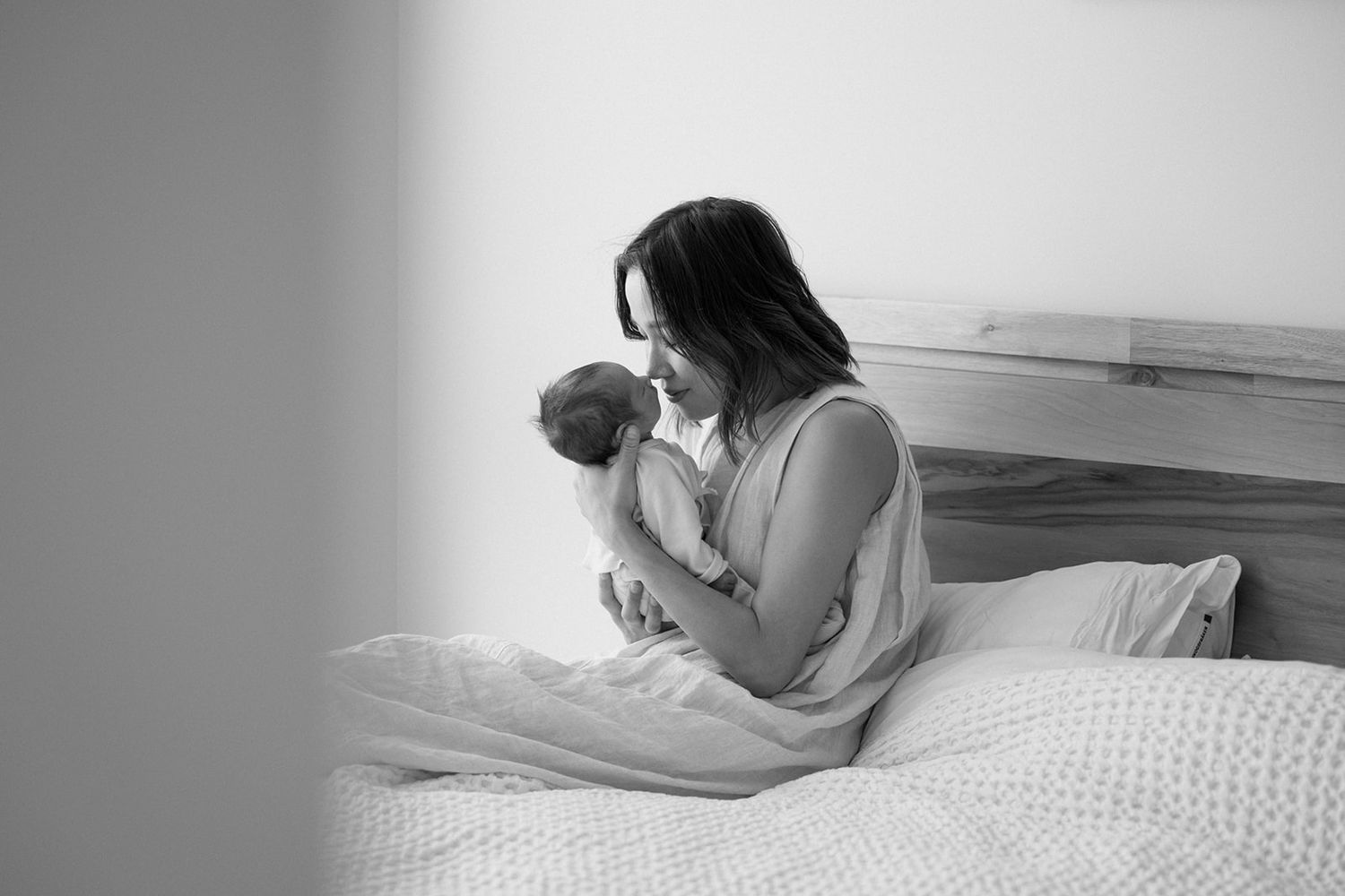 Mother cradling newborn baby on bed in intimate black and white photo.