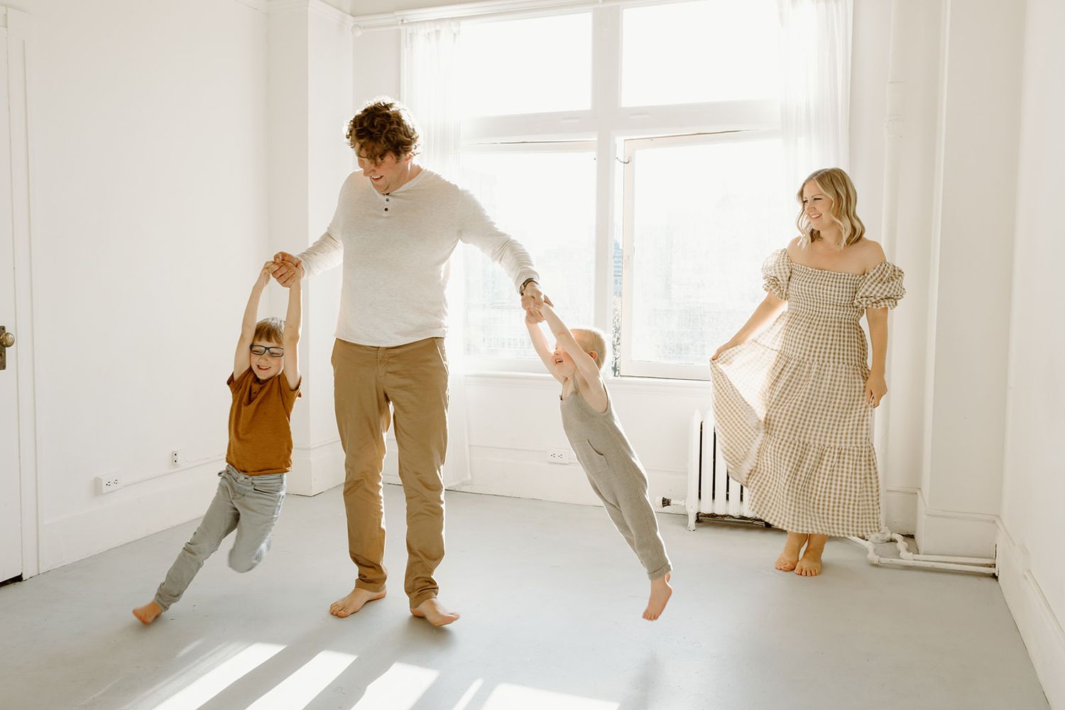 A family enjoying playful moments and dancing together in a bright white minimalist room.