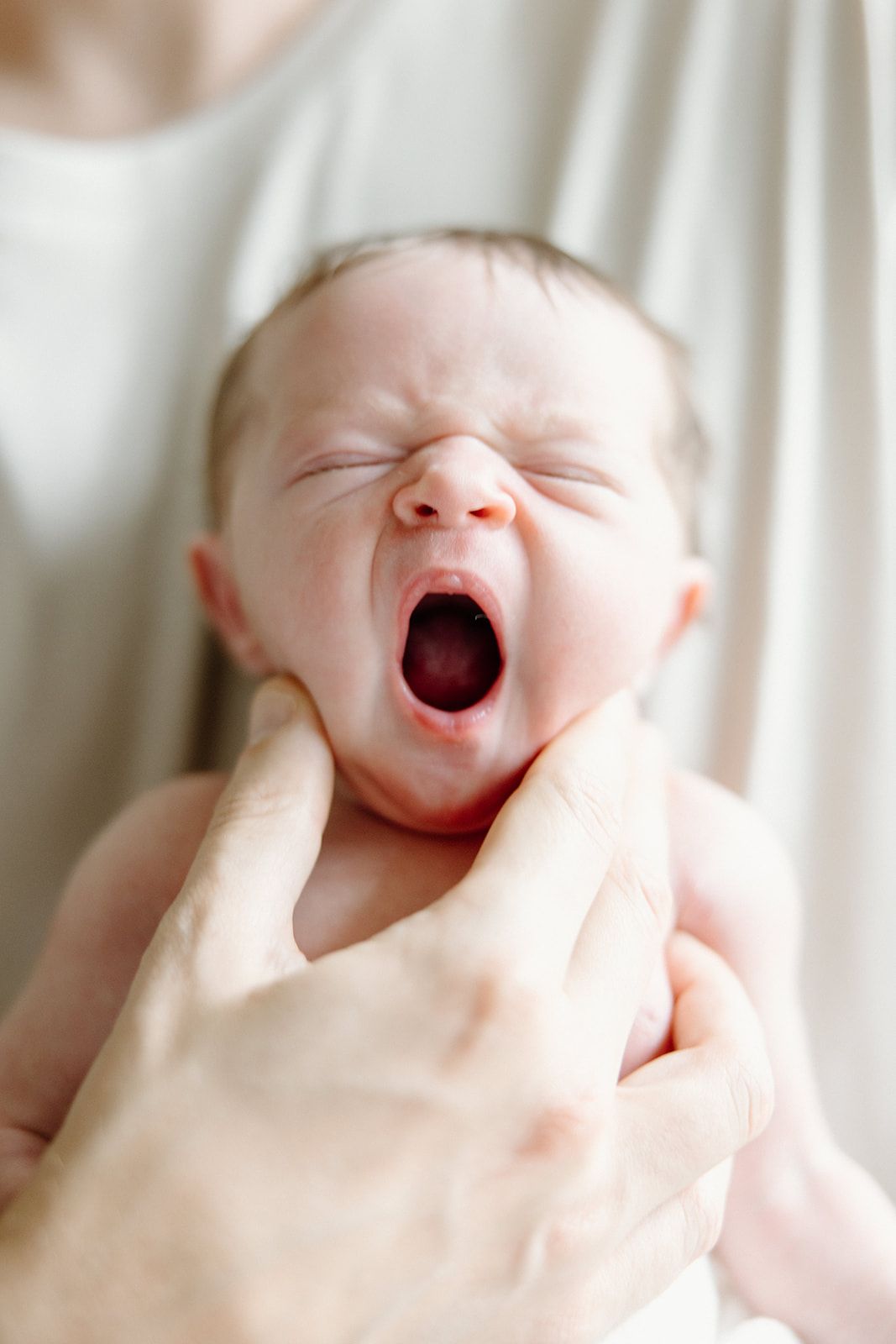 Sweet newborn baby yawning with mouth wide open against white background.