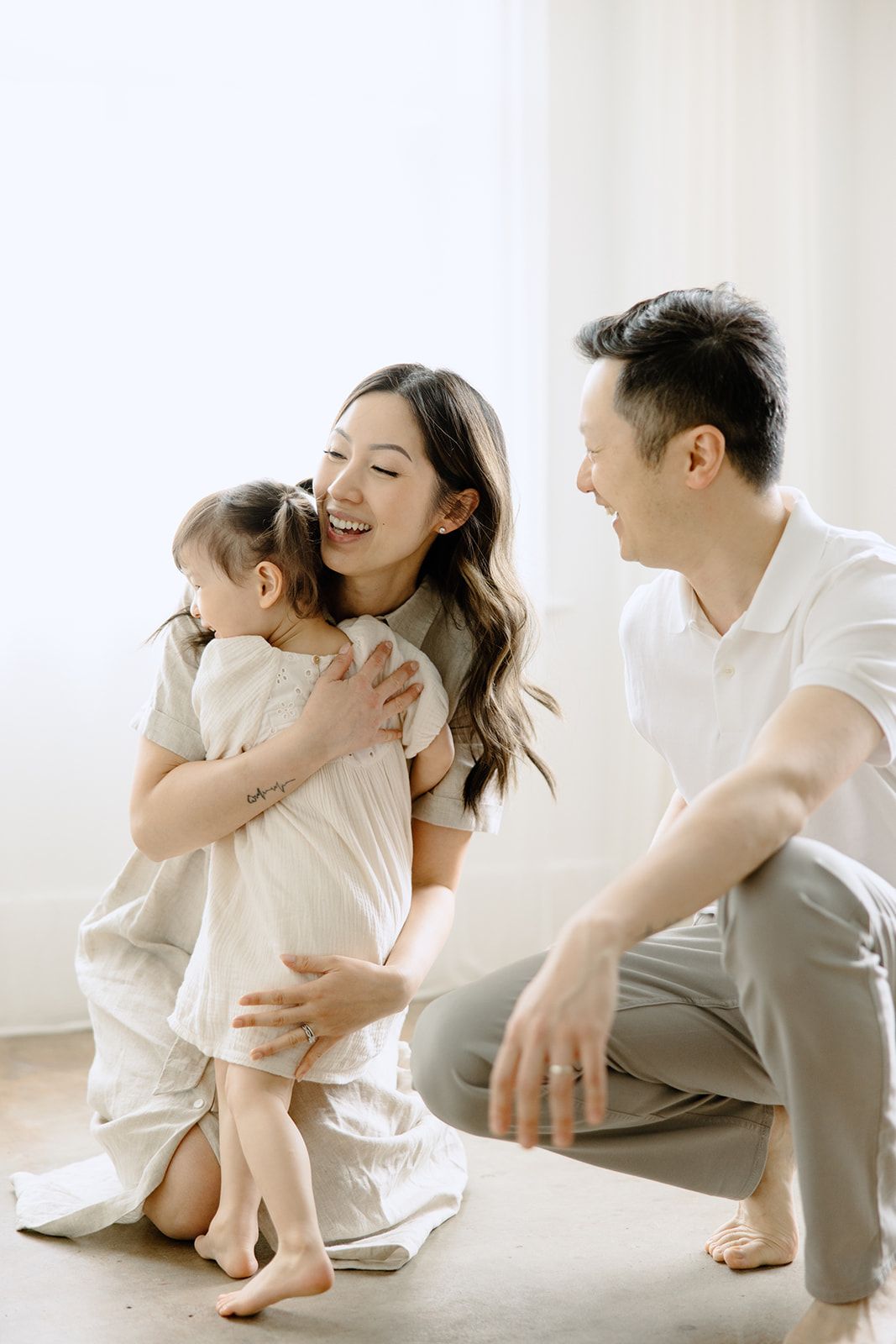 Family in white clothing sharing joyful moments together in a bright minimalist setting.