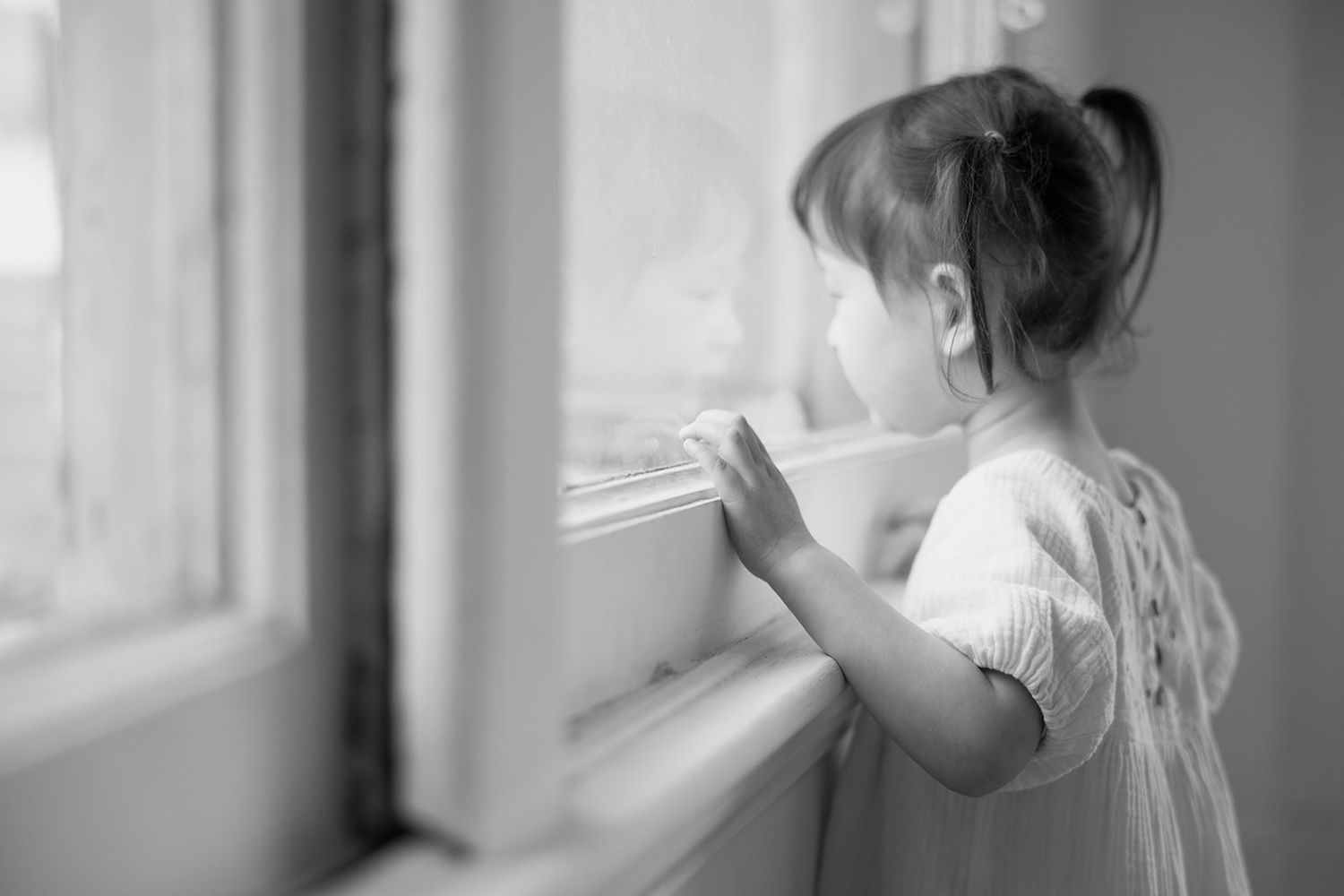 Young child looking through window with hands pressed against glass.