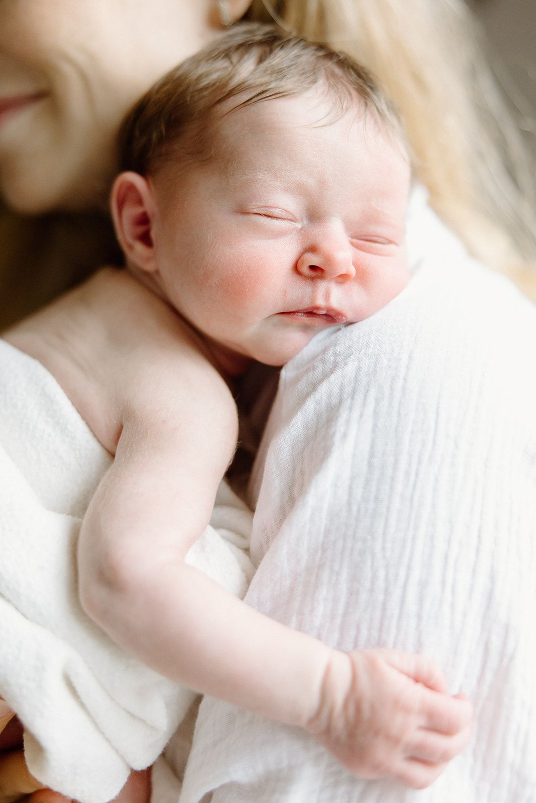 Peaceful sleeping newborn baby in white clothing lying against soft white bedding.