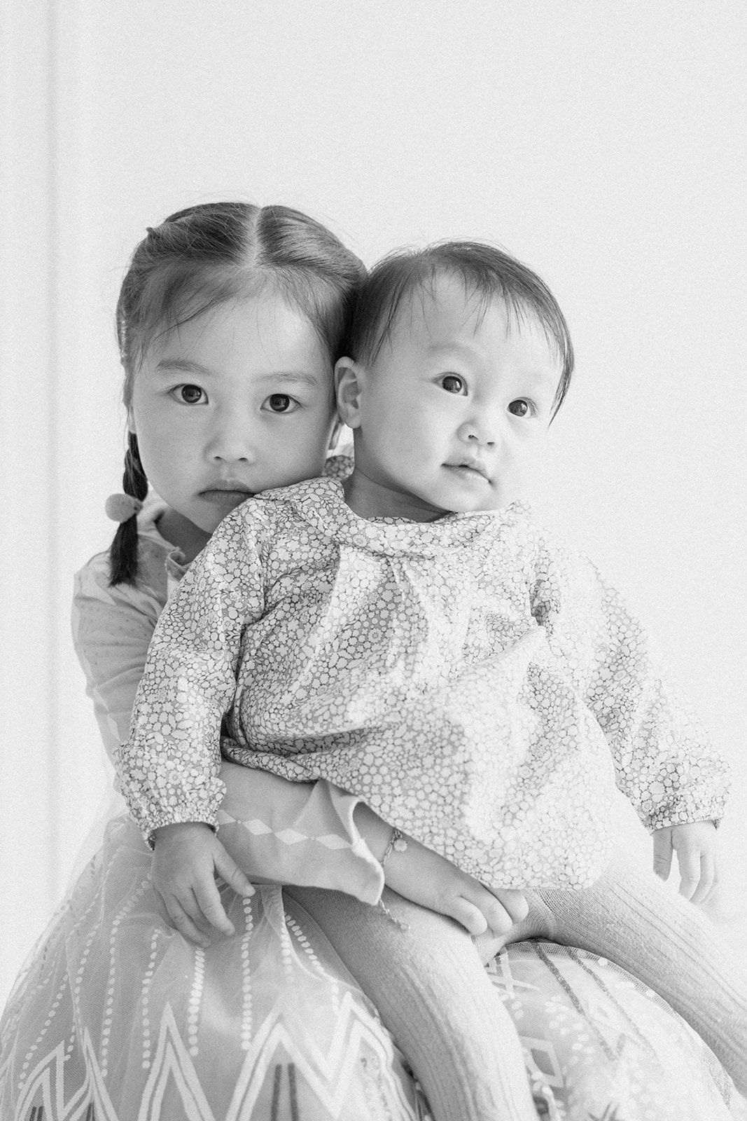 Two children in white sitting together against neutral background.