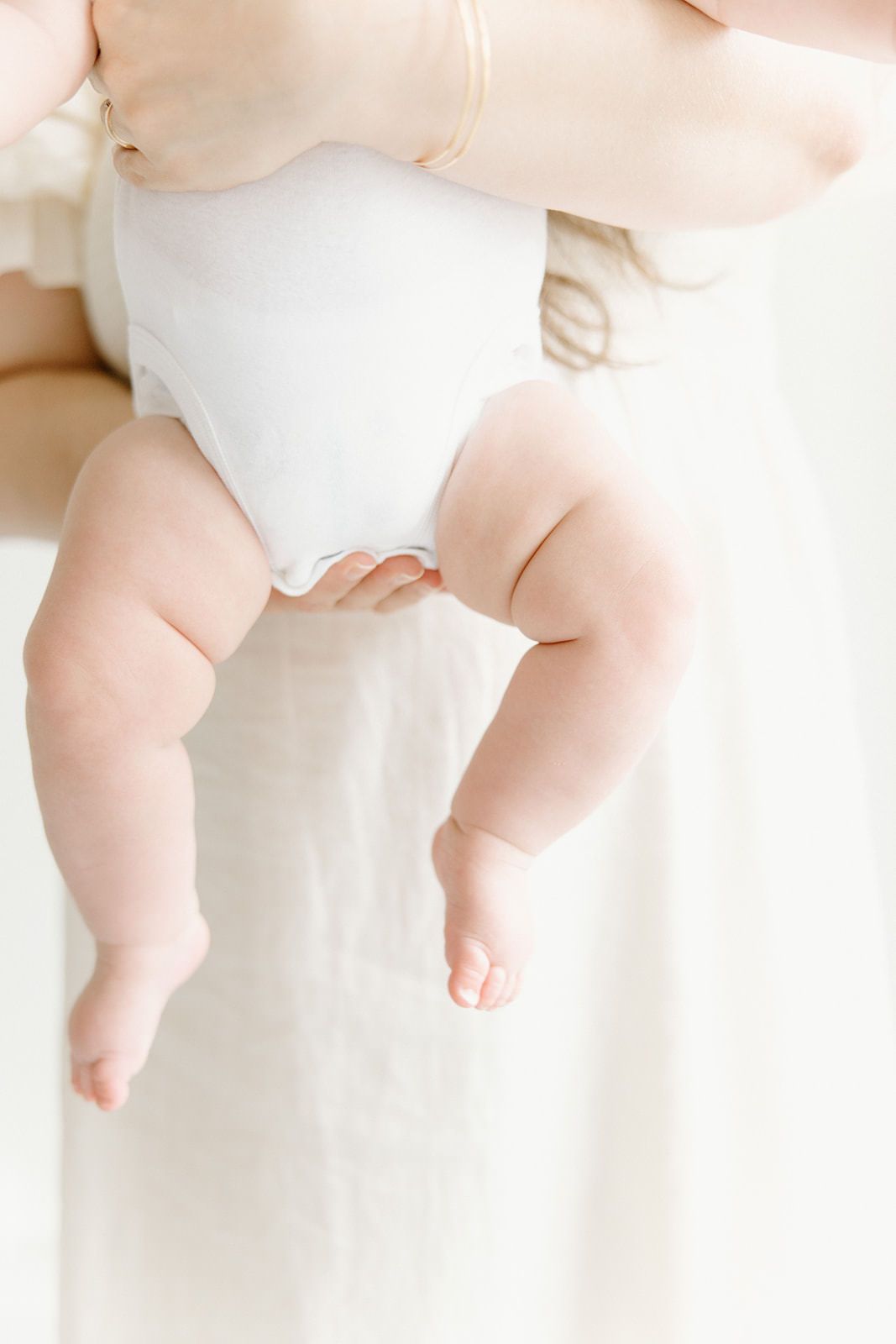 Close-up of tiny baby feet and legs against soft white background.