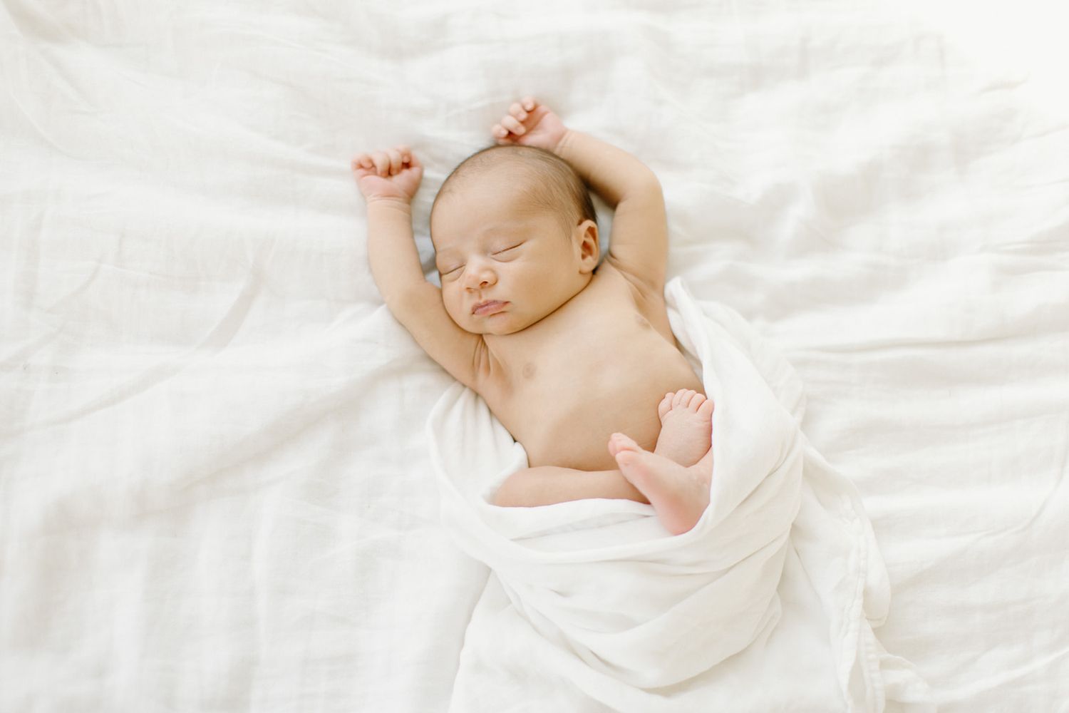 Sleeping baby in white bedding with natural lighting and soft focus creating a peaceful nursery scene.