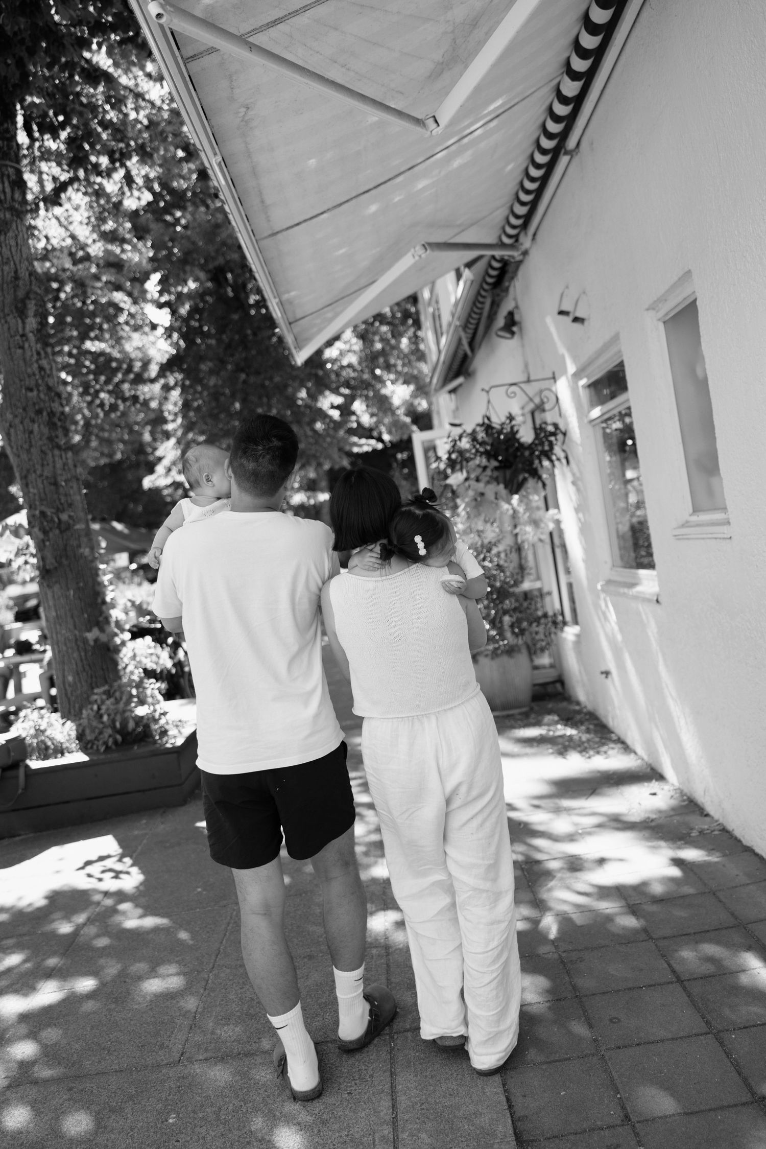 Black and white photo of two people walking together on a sunny sidewalk beside a building with an awning.